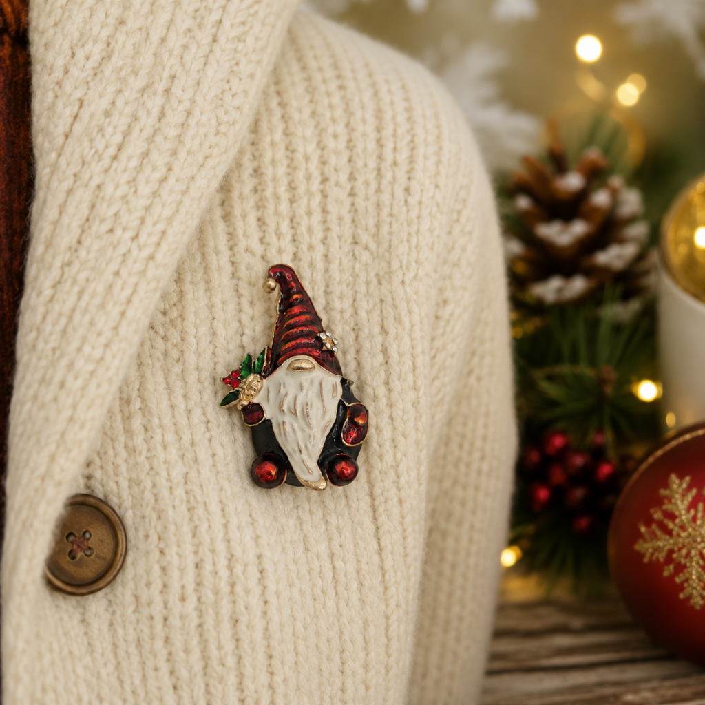 Festive Christmas gnome brooch with a red enamel hat, white beard and holly detail, pinned to a cosy cream knitted cardigan. Soft-focus Christmas decorations, pinecones and warm fairy lights create a welcoming holiday lifestyle scene.