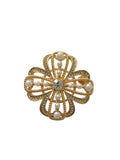 Pearl four-leaf clover brooch with central gemstone on a light gray background