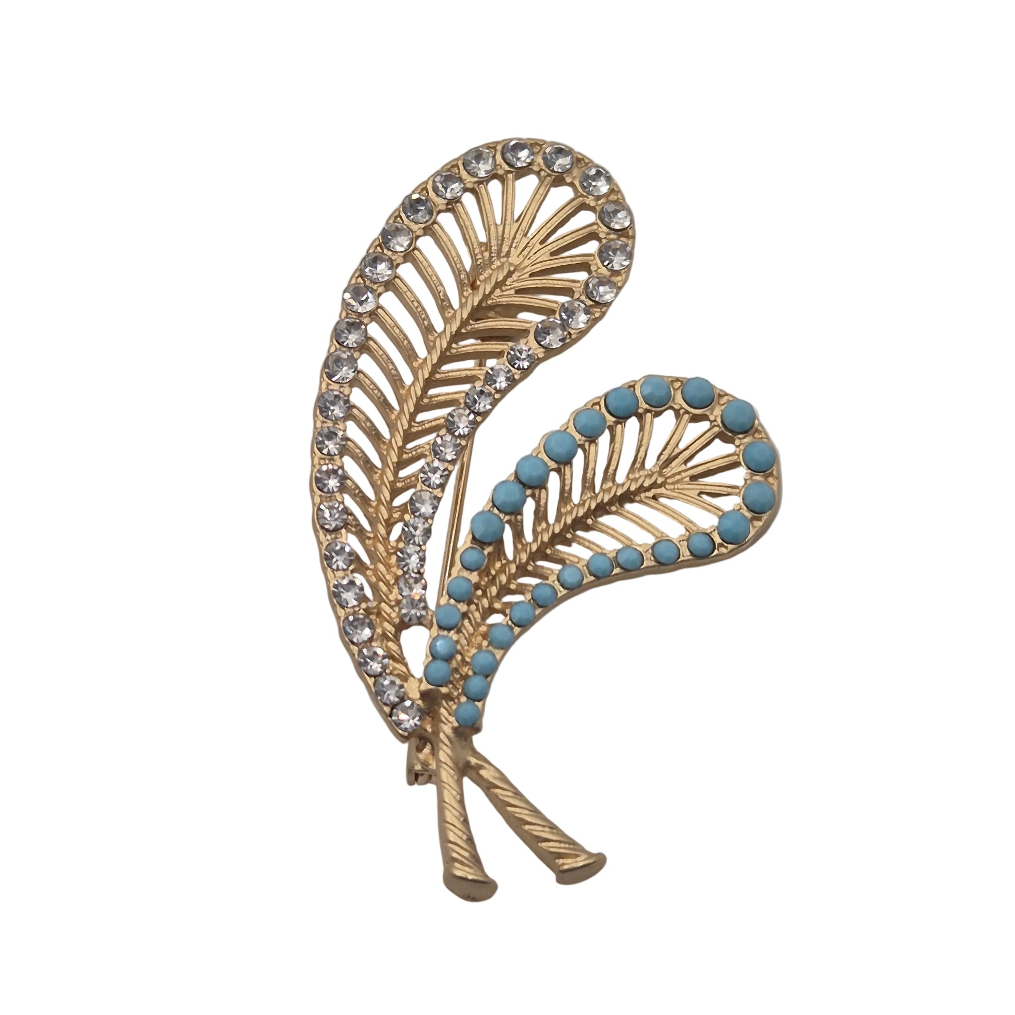 A gold-toned feather-shaped brooch decorated with clear rhinestones on one side and small light blue stones on the other, photographed on a plain light gray background.