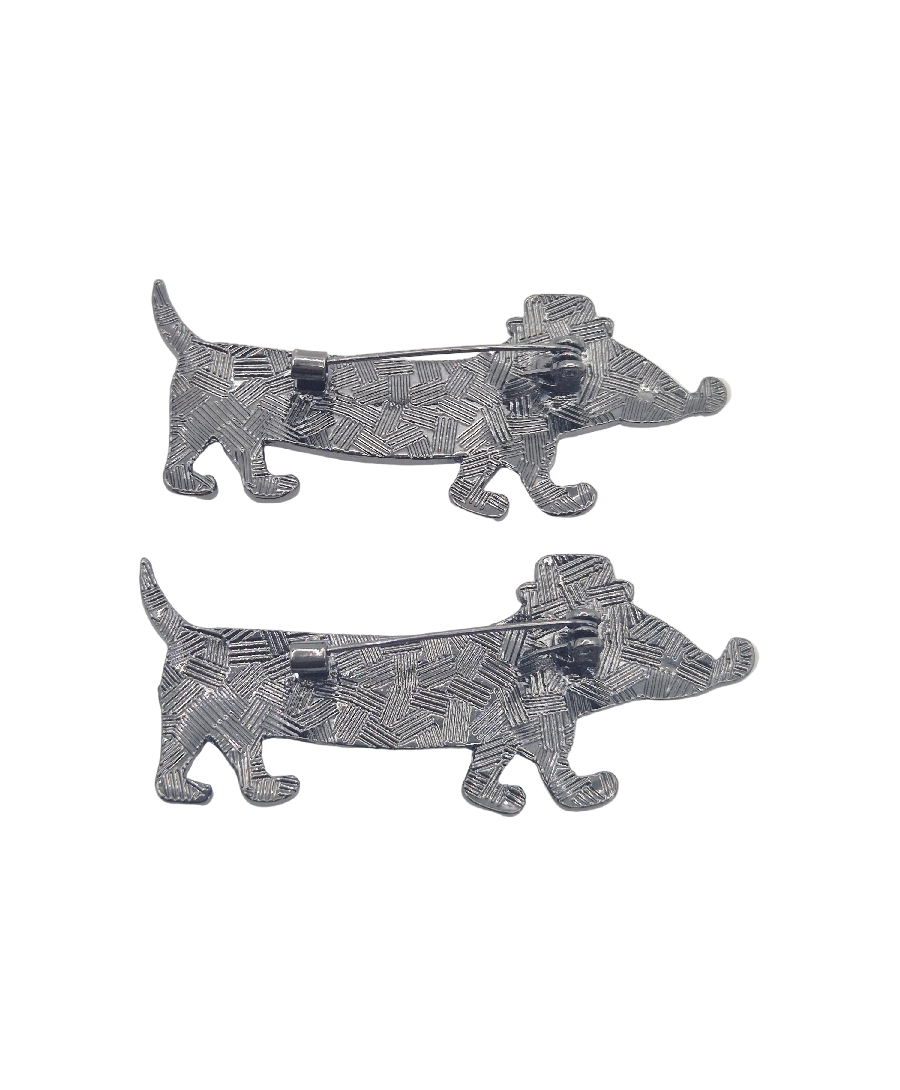 Reverse side of two metal dachshund dog brooches on a plain white background.