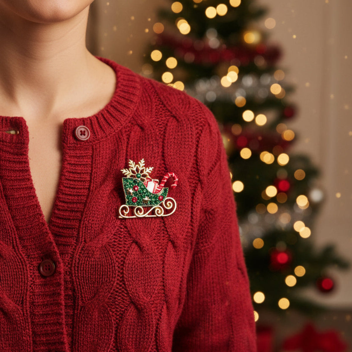 A Christmas-themed gold-tone enamel lapel pin depicting a sleigh filled with red and white striped candy canes, green glitter, and pink rhinestones, with a gold snowflake on top, set against a plain white background.