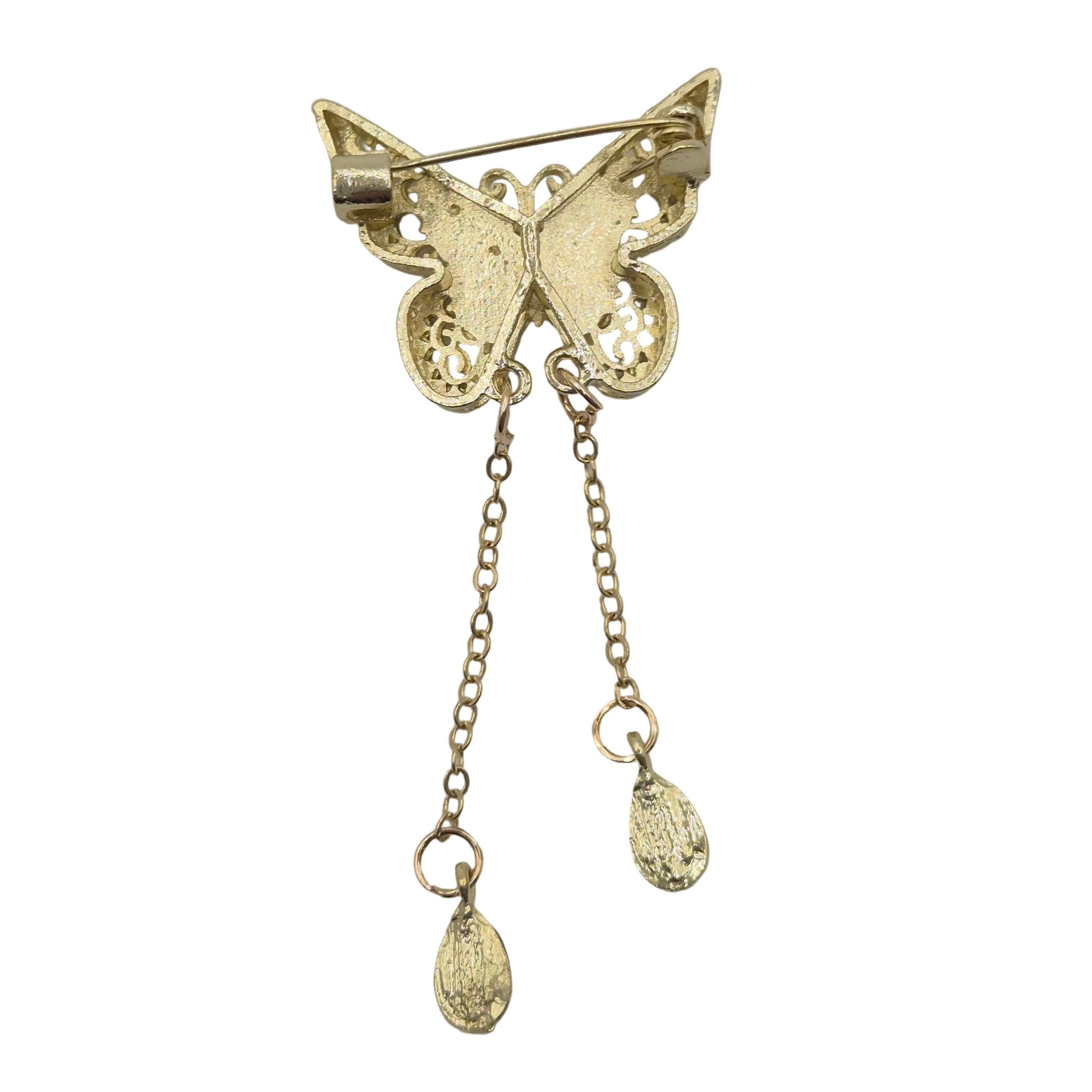 A gold butterfly-shaped brooch with intricate filigree detailing on the wings, featuring two dangling chain ends with small teardrop charms, photographed on a plain light gray background.