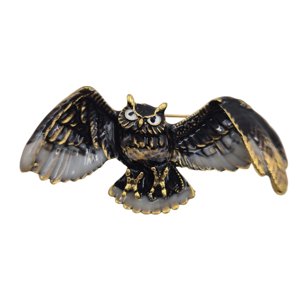 An owl-shaped brooch with spread wings, featuring a black enamel body and wings outlined in gold, with white and black eyes. Shown against a plain white background.