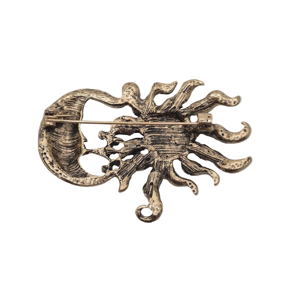An antique bronze sun and crescent moon brooch with a textured, oxidized finish, shown on a plain white background.