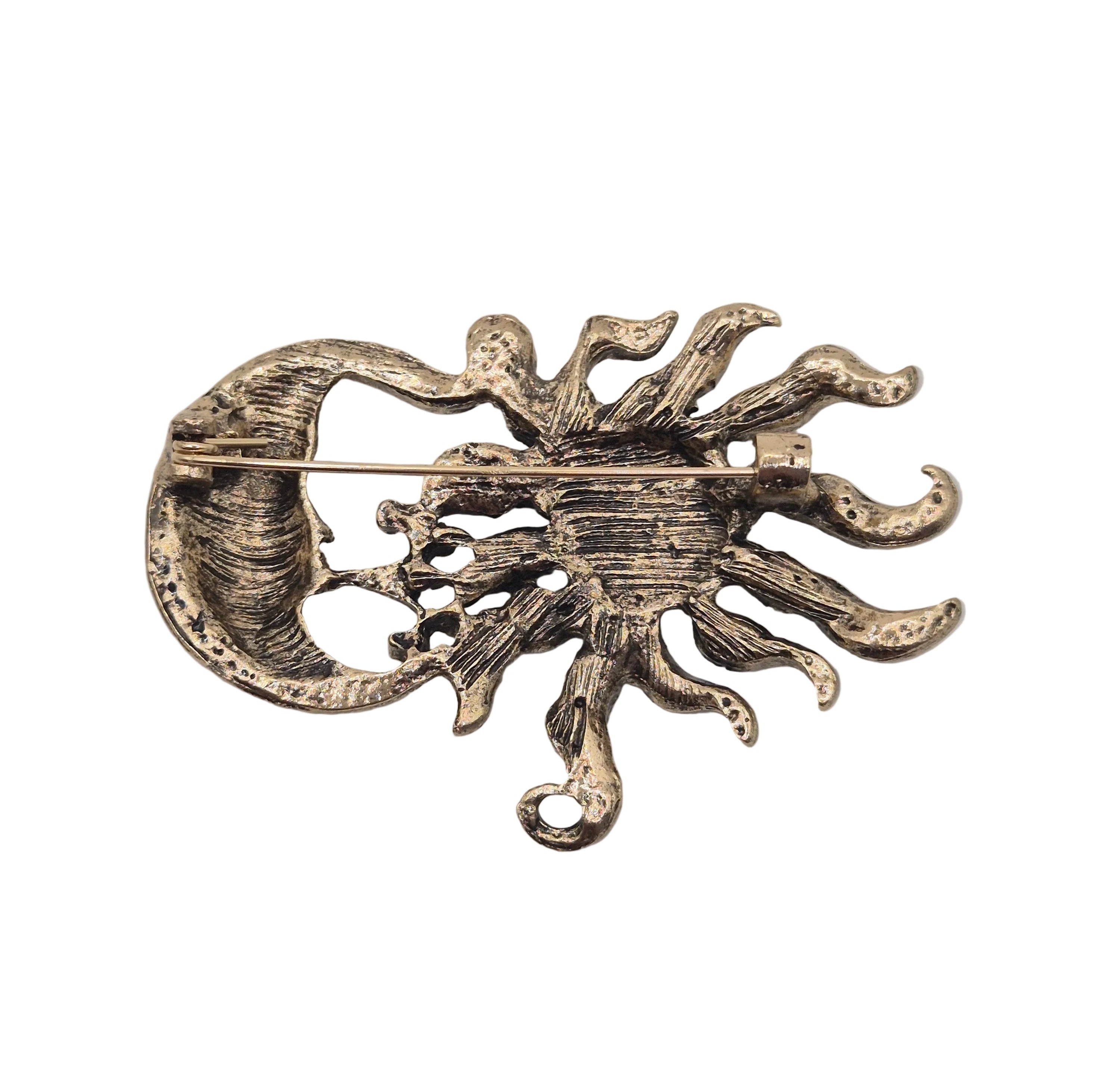 An antique bronze sun and crescent moon brooch with a textured, oxidized finish, shown on a plain white background.
