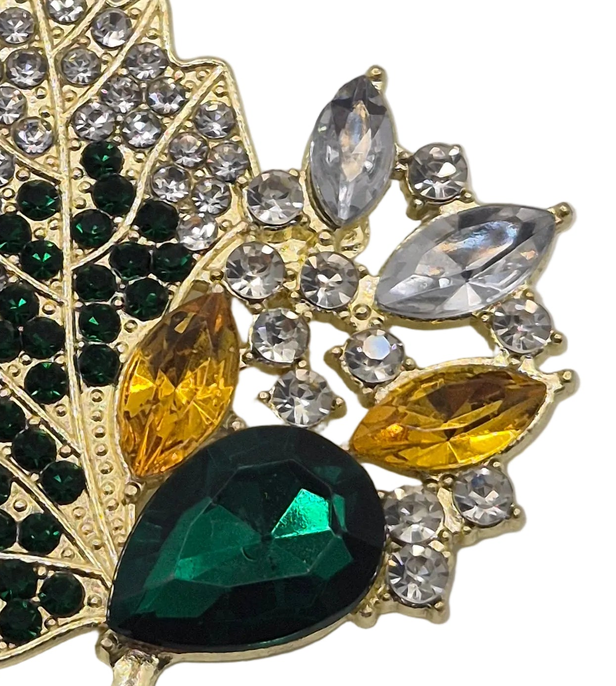 A close-up of a gold-tone brooch featuring faceted green and amber-yellow rhinestones, clear round crystals, and a large dark green teardrop stone on a white background.