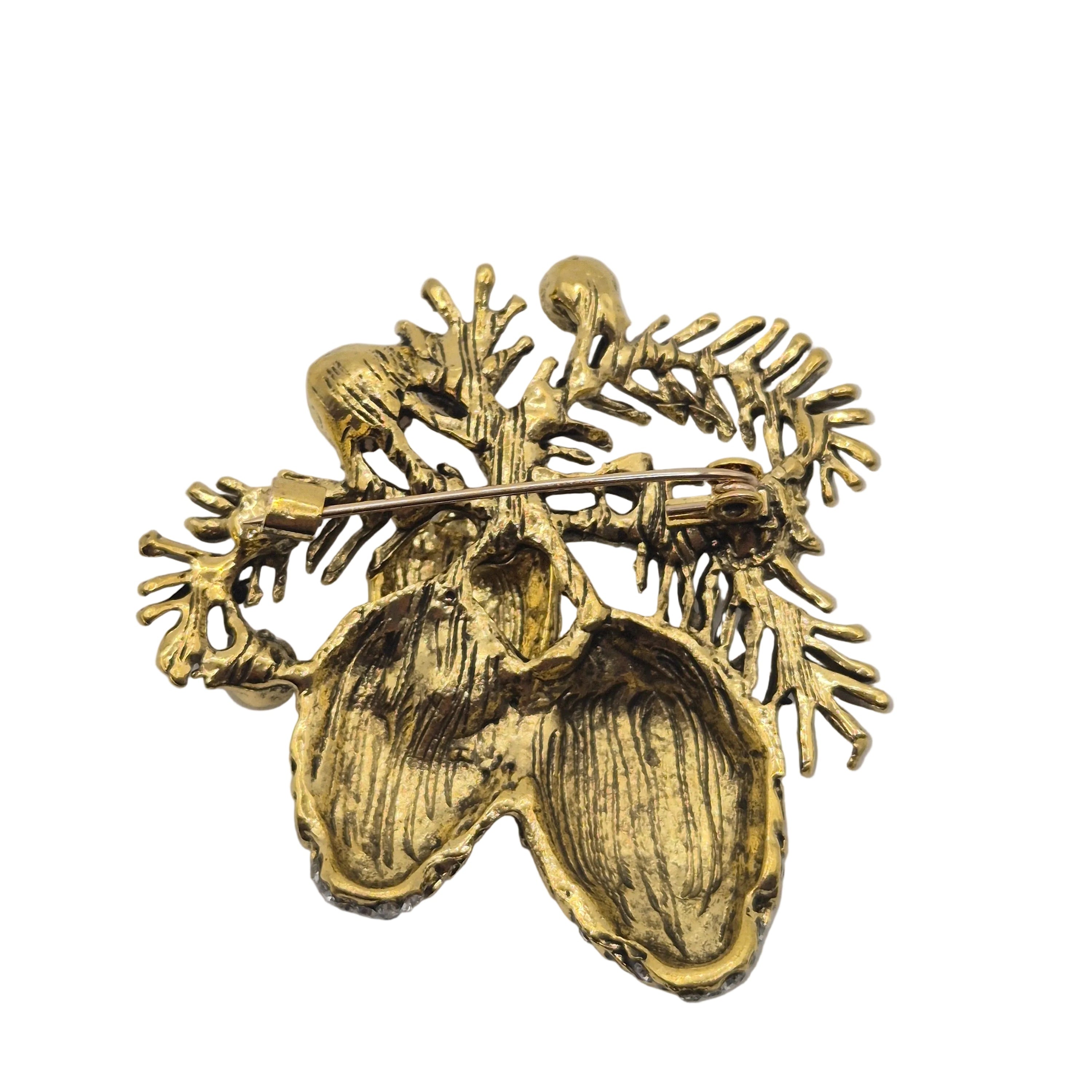 A gold-tone textured brooch featuring a pineconel design with leaf-like branches and a central heart-shaped motif, shown against a plain white background.