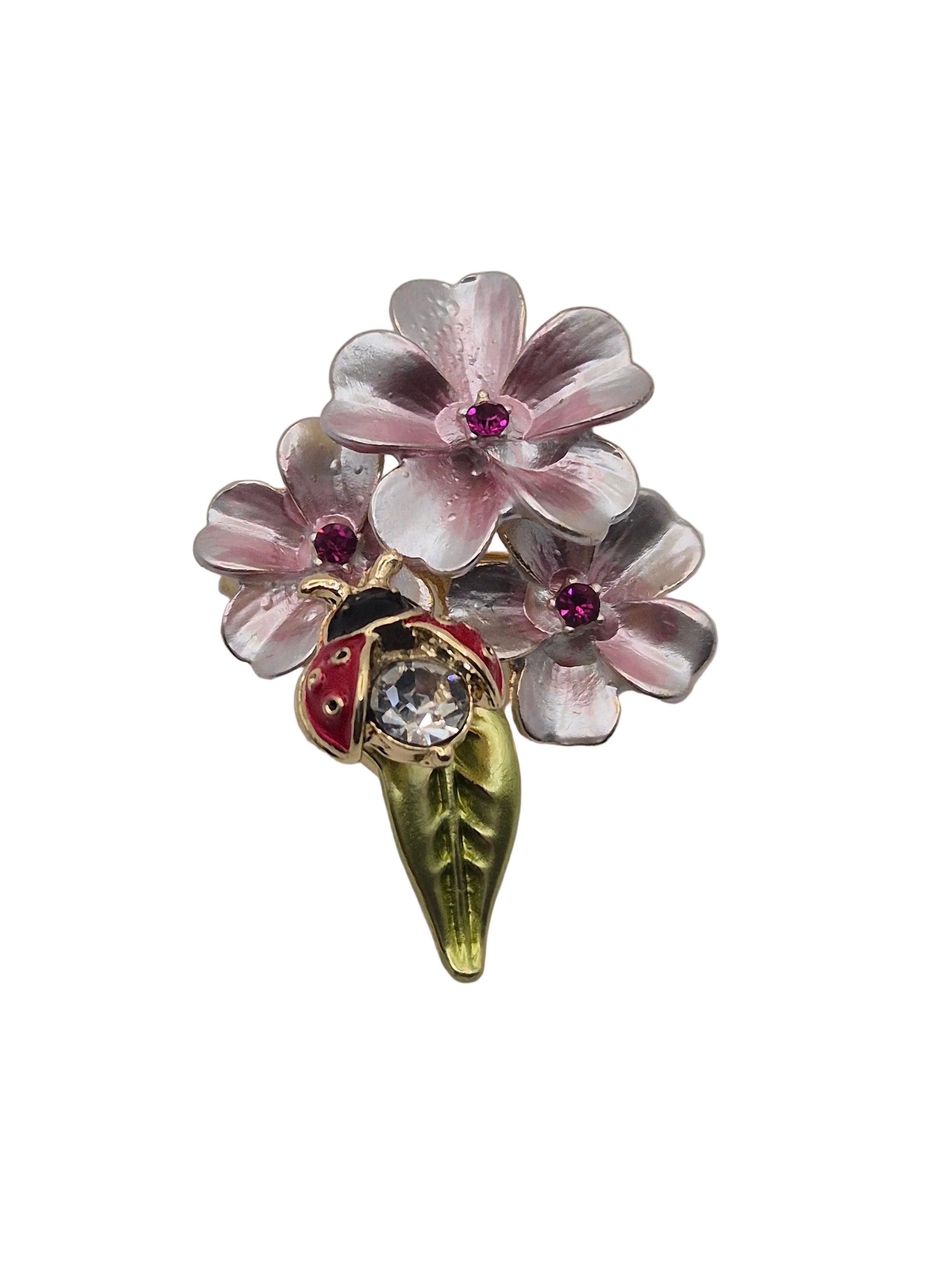 A vintage-style enamel brooch featuring three light pink cherry blossoms with purple centers, a small red ladybug with black spots, and a green leaf stem, set against a plain white background.