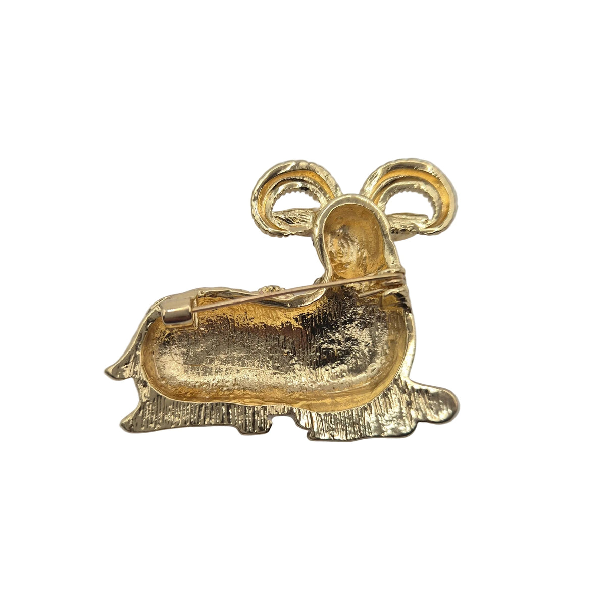 A gold-coloured metal ram shaped brooch showing the reverse side and pin mechanism. Shown on a plain white background.