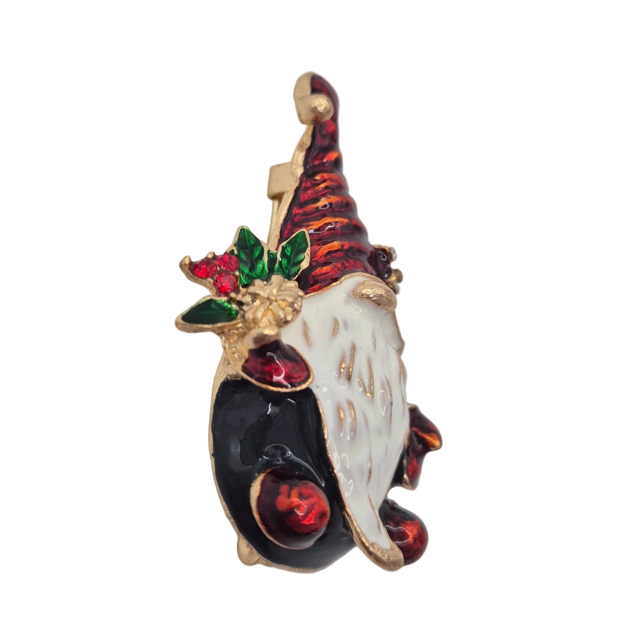 A Christmas gnome brooch featuring a white beard, a red and black striped hat, a black body, and green and red holly accents, set in gold-tone metal against a plain white background.