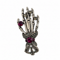 A gothic skeleton hand brooch in antique silver-tone metal, adorned with faceted dark red gemstones and small clear rhinestones, shown on a plain white background.
