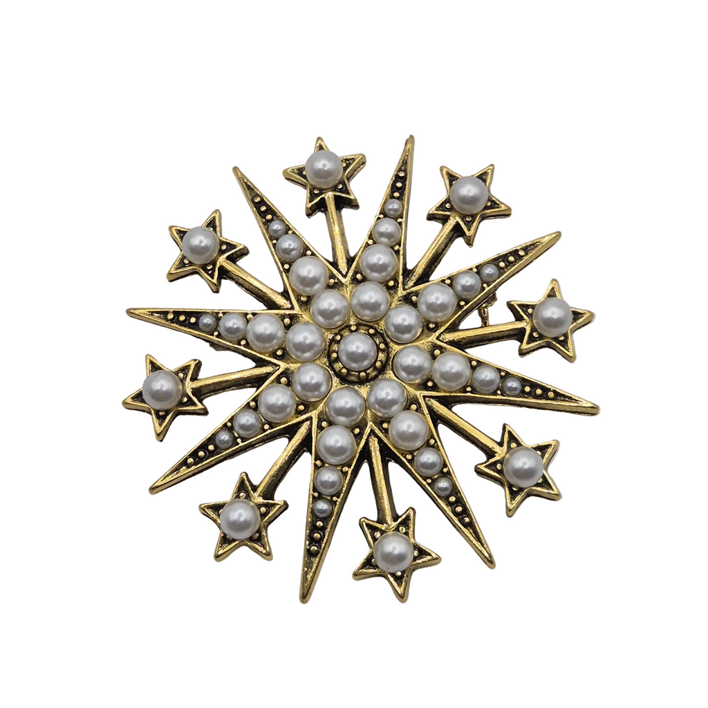 A gold starburst brooch decorated with white pearls and small black-set accents, isolated on a white background.