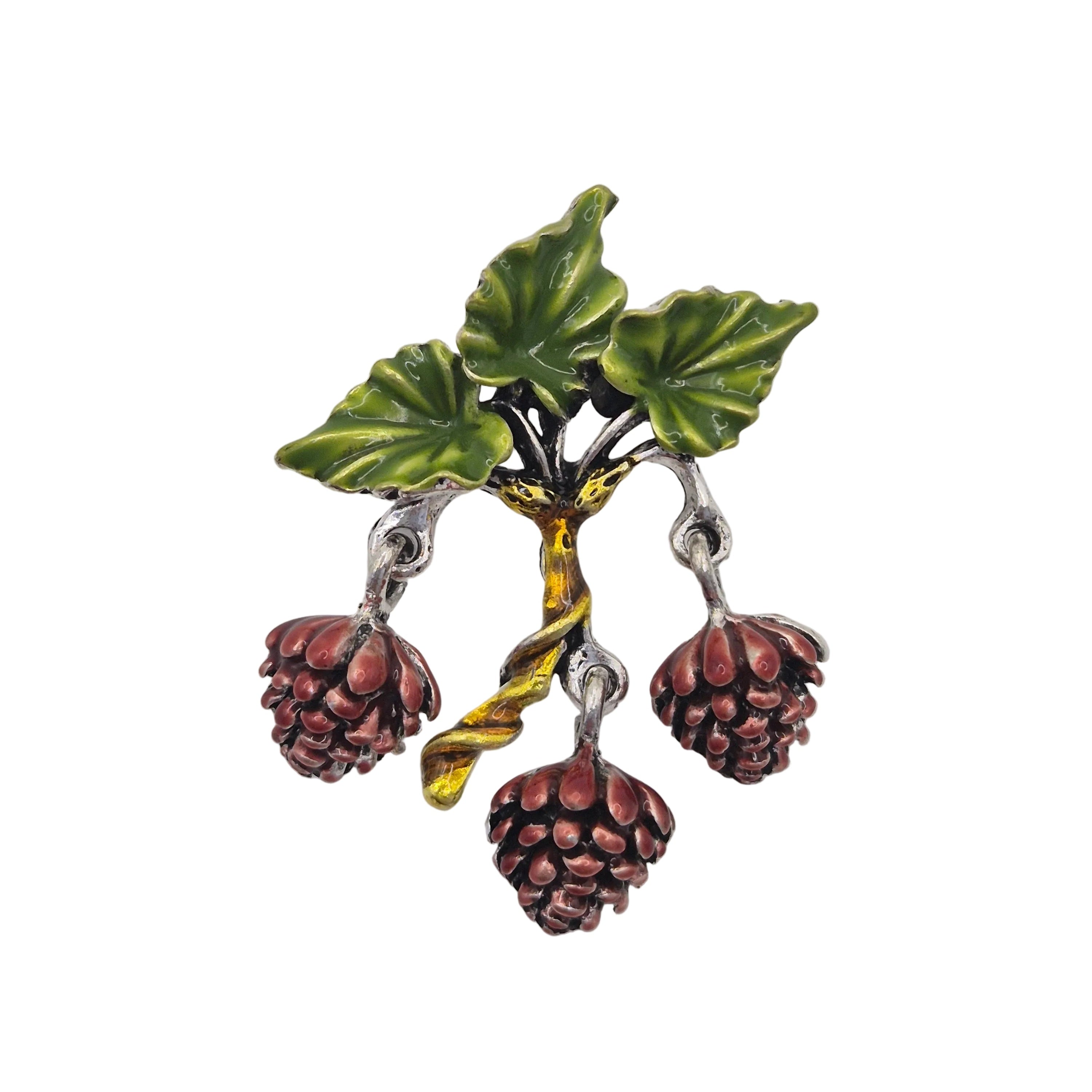 A vintage-style enamel brooch shaped like a branch with pinecones, green leaves, a yellow-green stem, and three dangling brown pinecones on silver-tone metal.