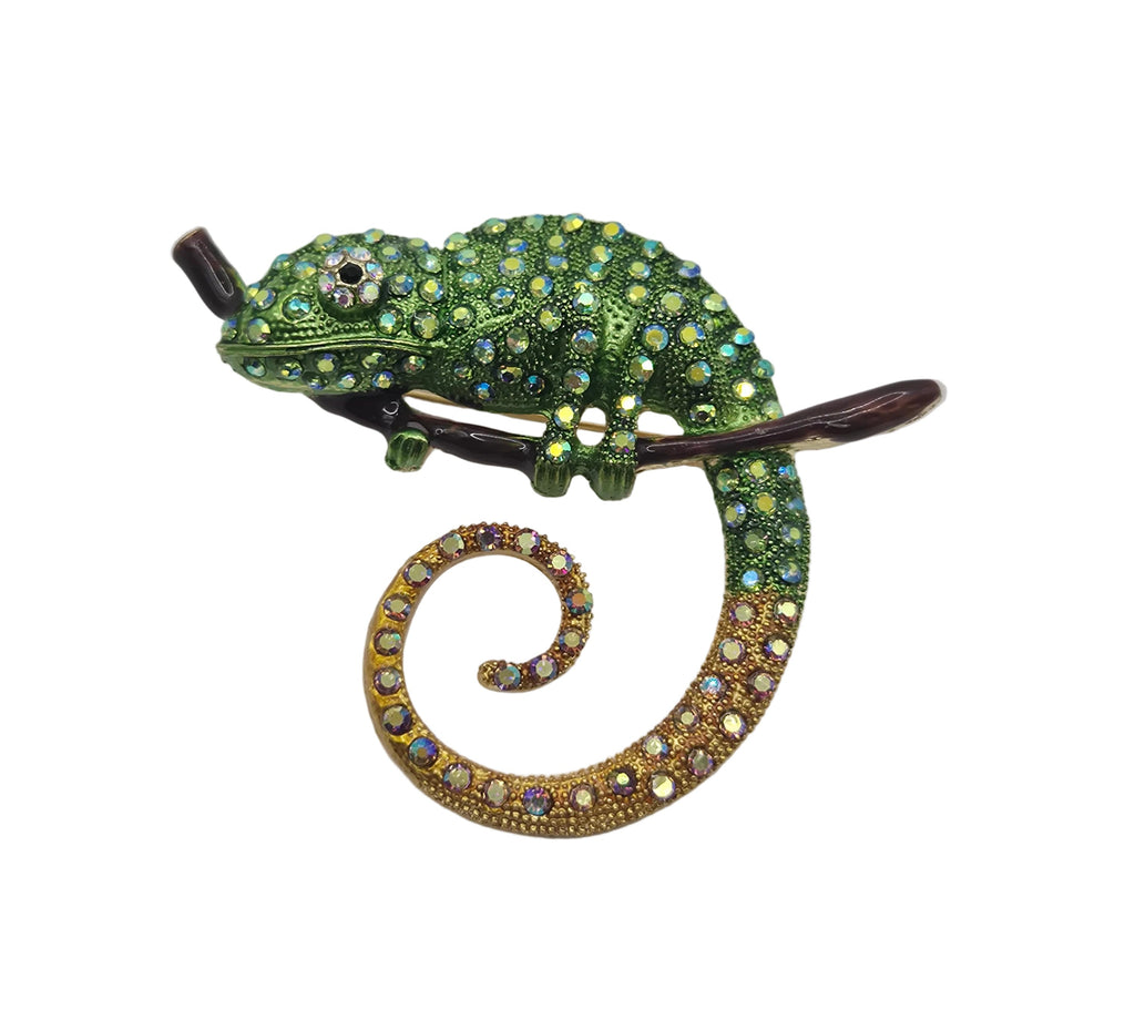 A decorative lizard or chameleon-shaped brooch embellished with green rhinestones and a gold-toned curled tail, photographed on a plain white background.