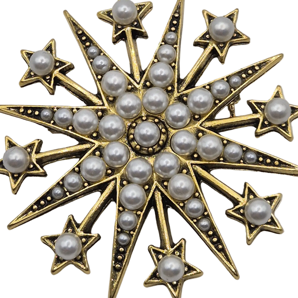 A gold-toned starburst brooch decorated with multiple white faux pearls, shown against a plain white background.