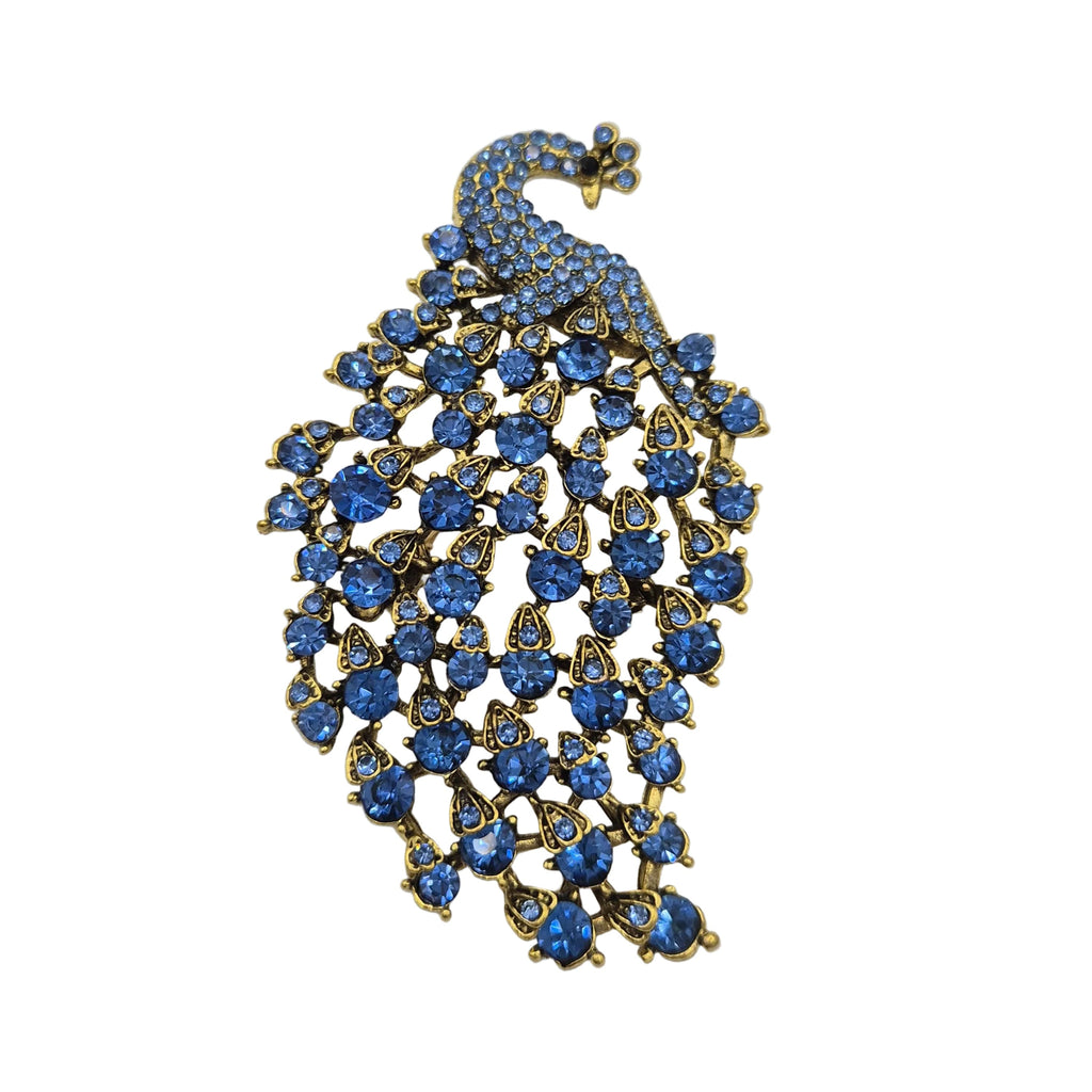 A peacock-shaped brooch featuring blue rhinestones set in gold-tone metal, displayed on a plain white background.