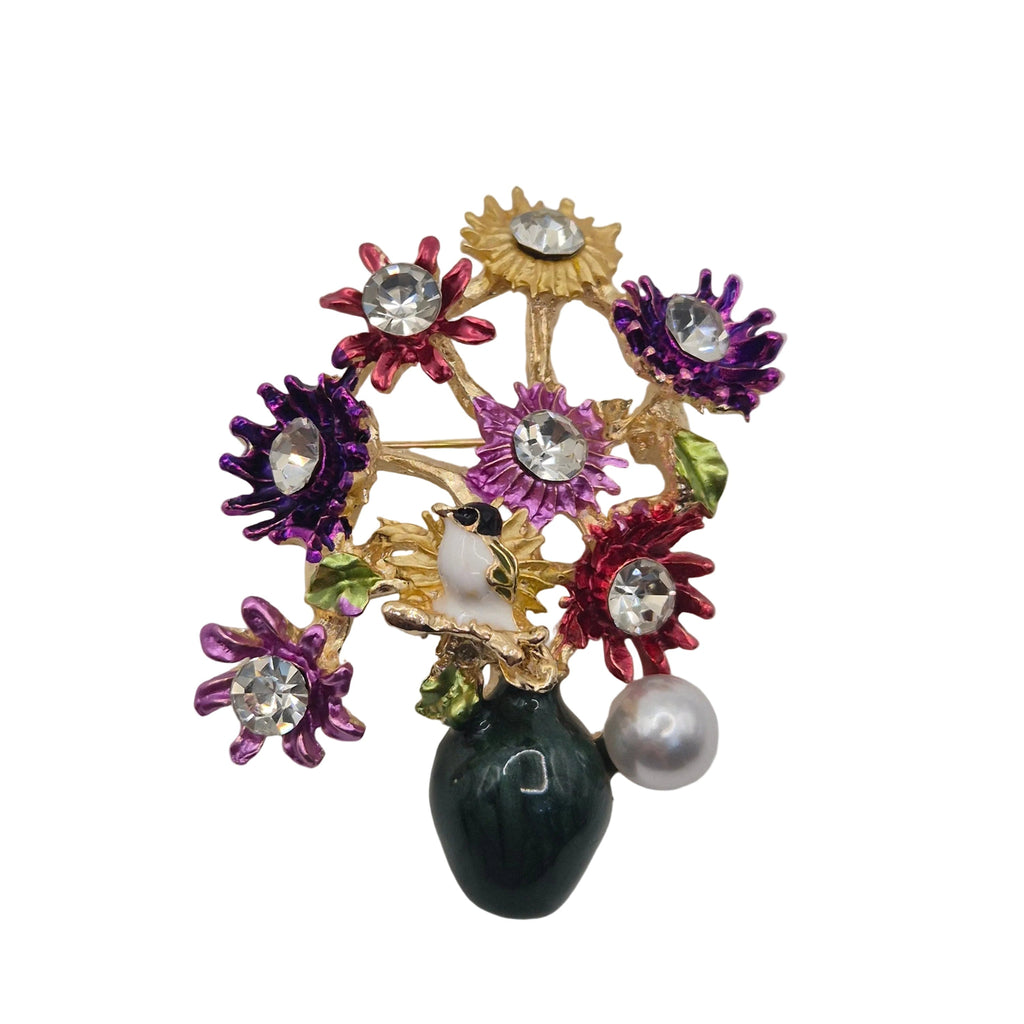 A vintage-style floral enamel brooch featuring gold-tone metal, purple, red, and yellow enamel flowers, clear rhinestones, a white pearl, and a dark green teardrop-shaped bead on a plain light gray background.