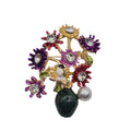 A vintage-style floral enamel brooch featuring gold-tone metal, purple, red, and yellow enamel flowers, clear rhinestones, a white pearl, and a dark green teardrop-shaped bead on a plain light gray background.