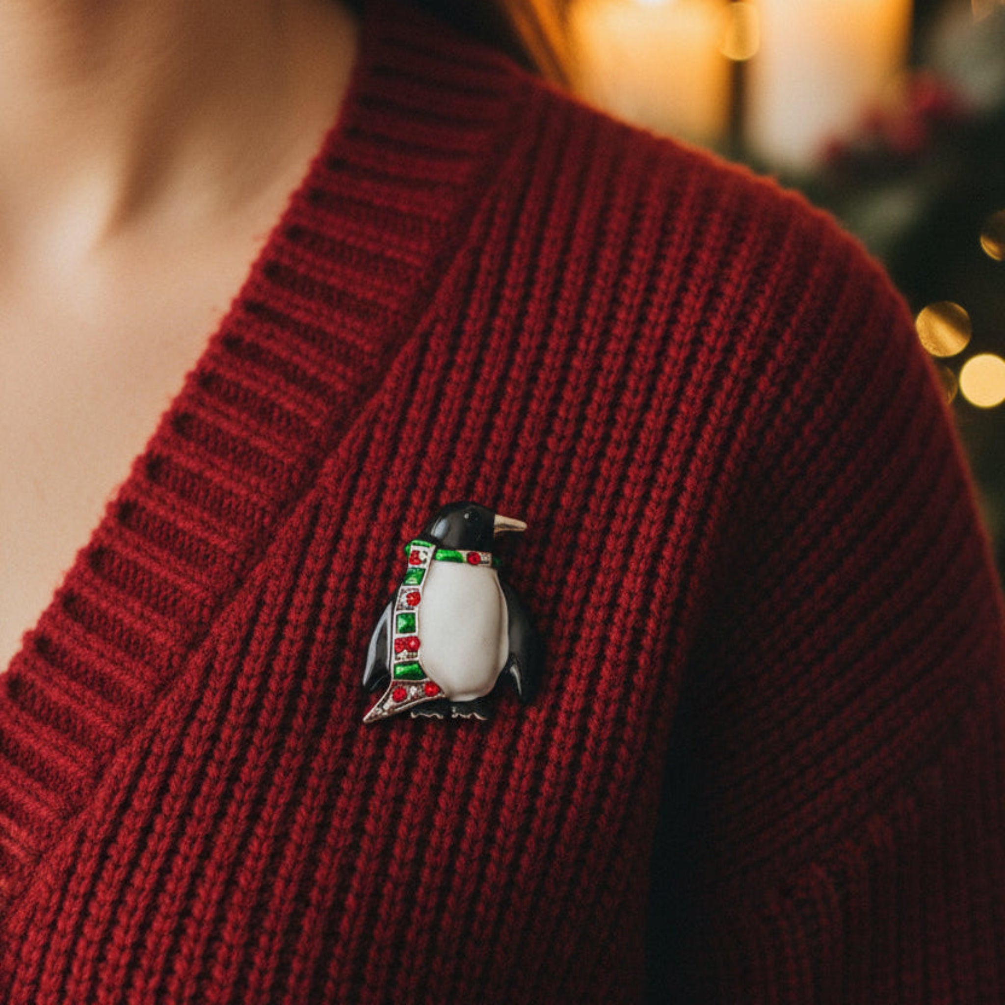 A penguin-shaped brooch with a glossy white belly, black wings and head, a silver beak and outline, and a green scarf embellished with red rhinestones, shown on a plain white background.