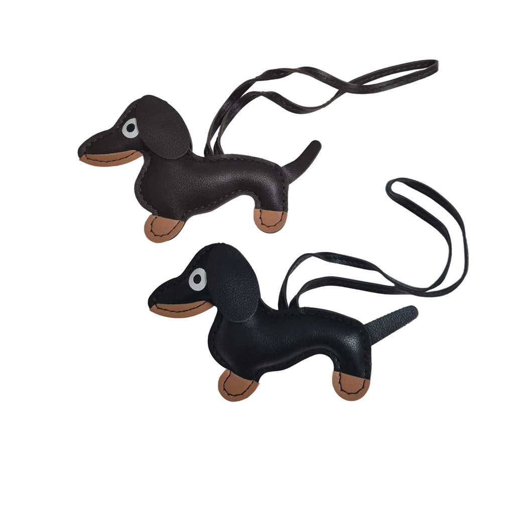 Two faux leather dachshund-shaped bag charms with brown paws and snouts, each attached to a black strap, shown on a plain white background.