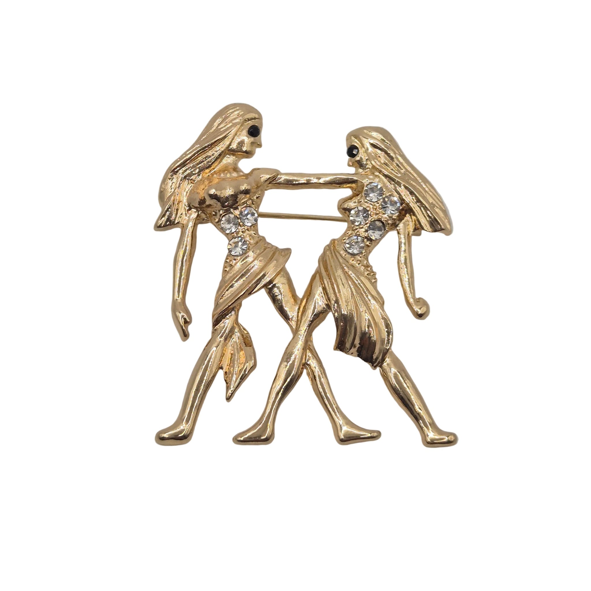 A gold tone Gemini zodiac sign brooch with rhinestone detail, depicting two women. Shown against a plain white background.