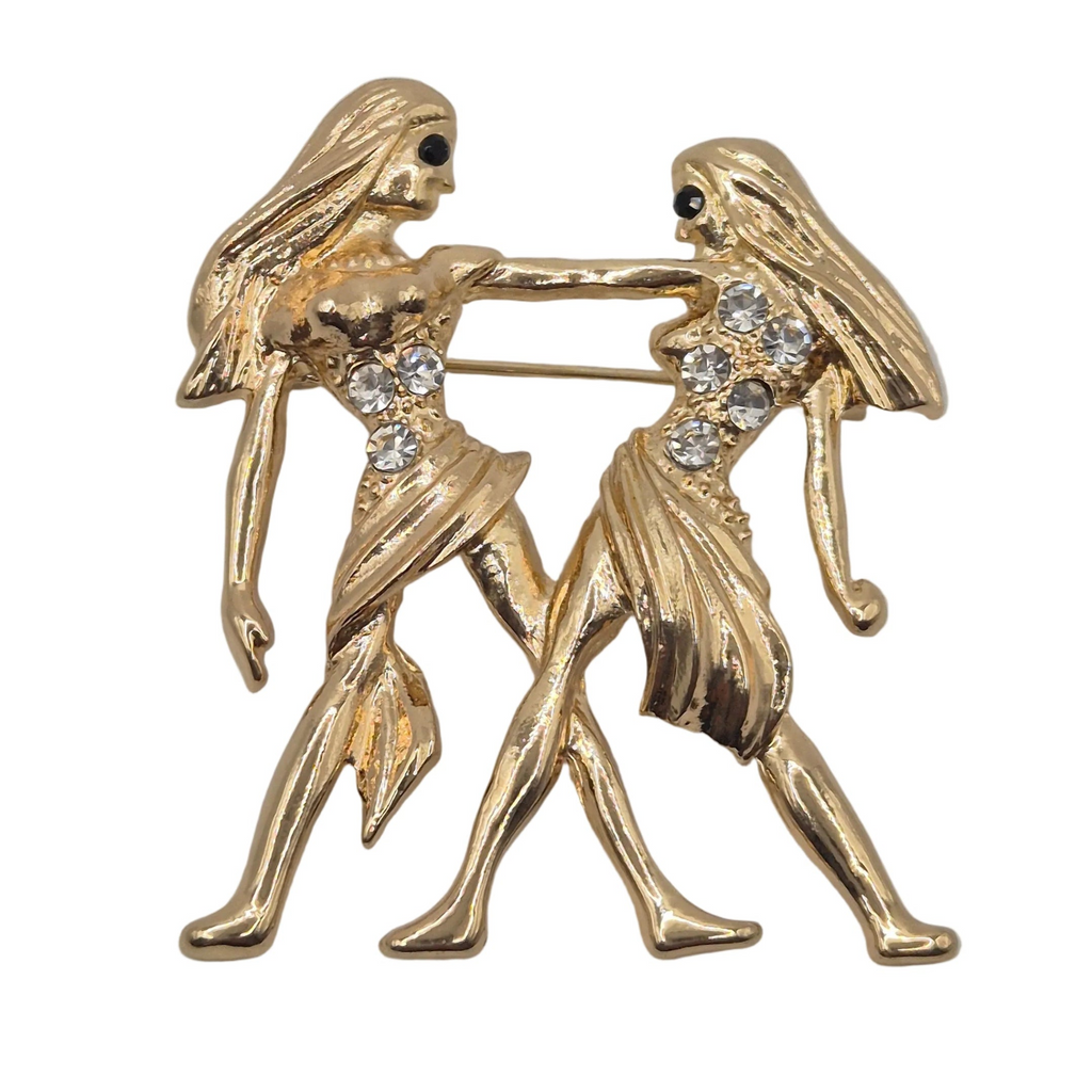 A gold tone Gemini zodiac sign brooch with rhinestone detailing. Shown against a plain white background.