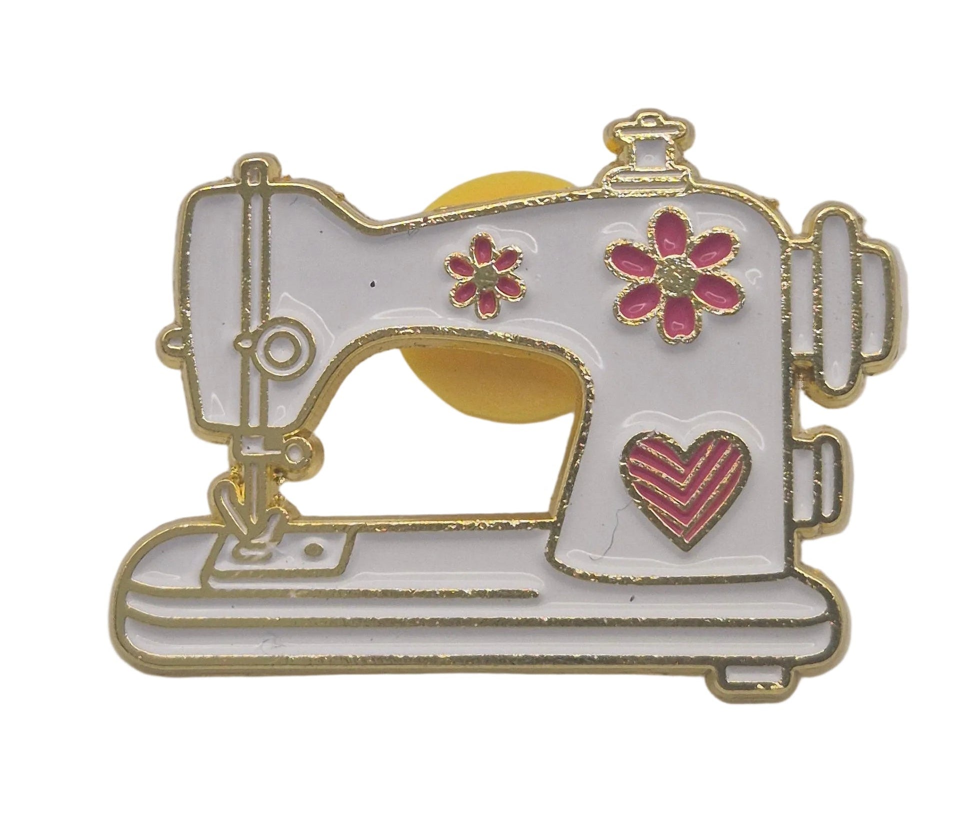 A small enamel pin shaped like a sewing machine, with a white body, gold-tone metal outline, pink floral details, and a pink heart on a white background.