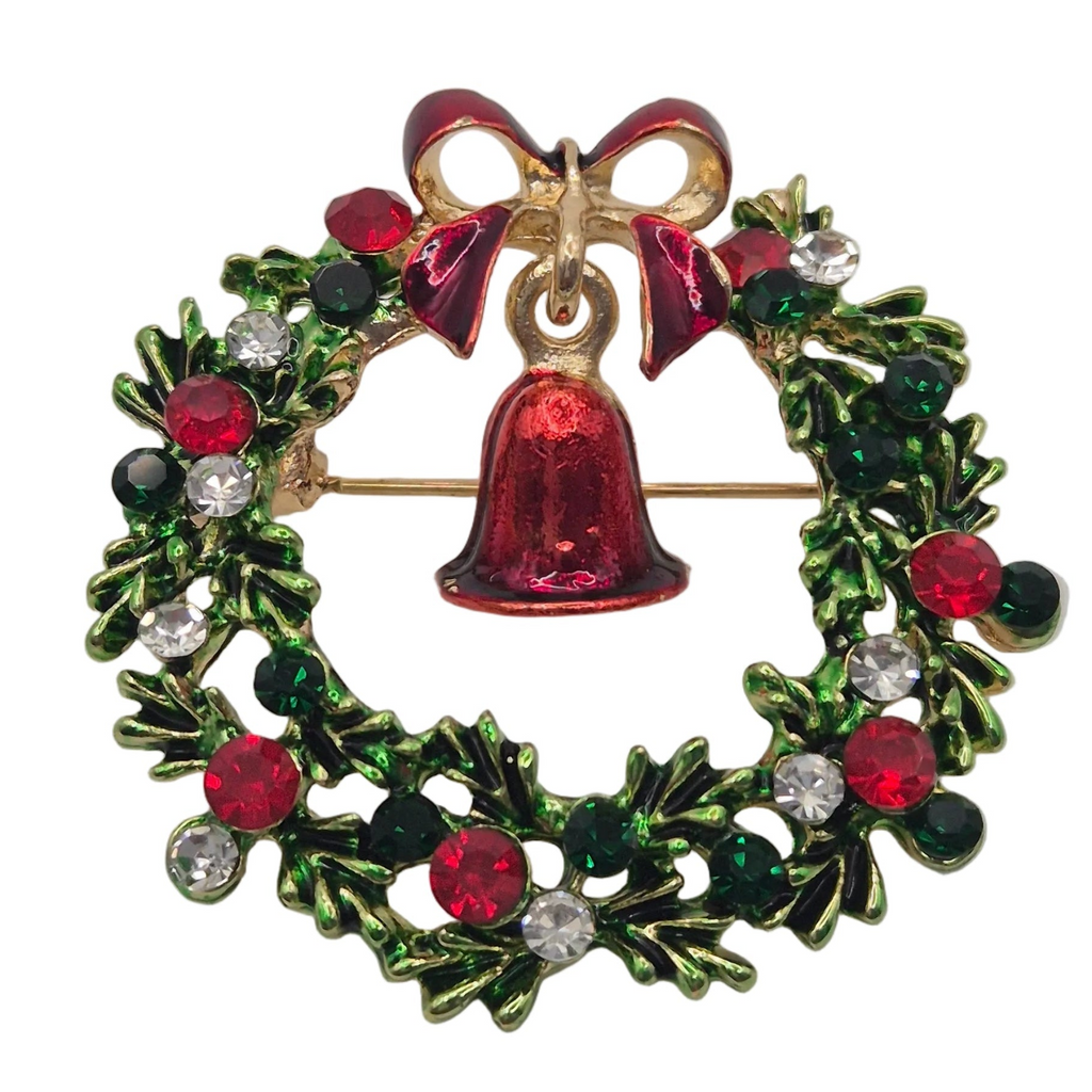 A Christmas wreath brooch featuring a red enamel bell, red bow, green and red enamel holly leaves, and clear and dark rhinestones on a gold-tone base.