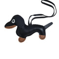 A black faux-leather dachshund-shaped keychain or bag charm with tan accents on the muzzle, paws, and inner ears, plus a black strap, photographed on a plain white background.