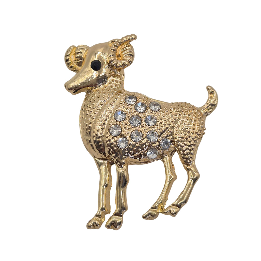 A gold-colored ram brooch decorated with clear rhinestones on its body, set against a plain white background.