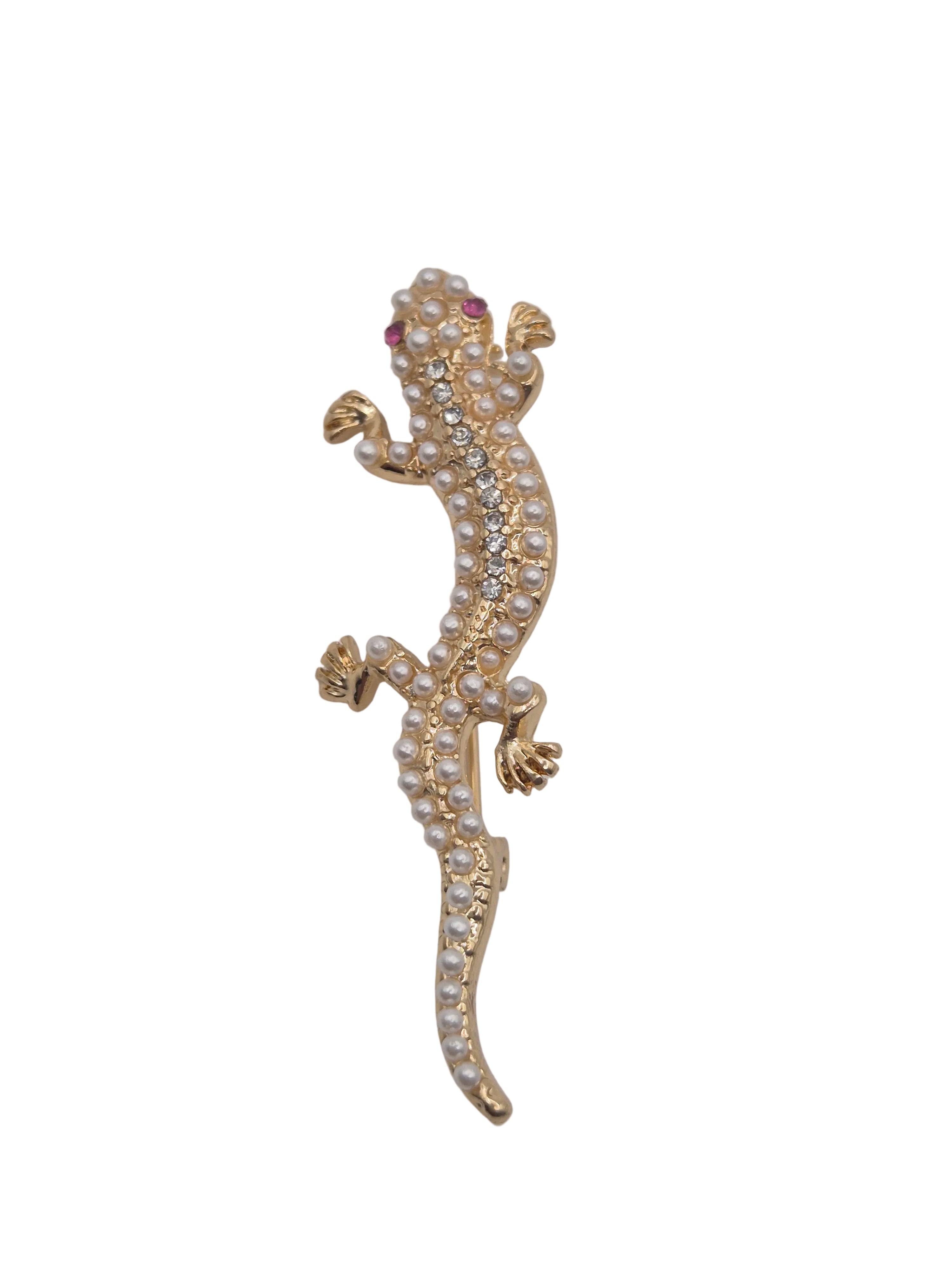 A gold gecko or lizard-shaped brooch embellished with small white pearls and clear rhinestones, featuring tiny red gemstone eyes, shown against a plain white background.