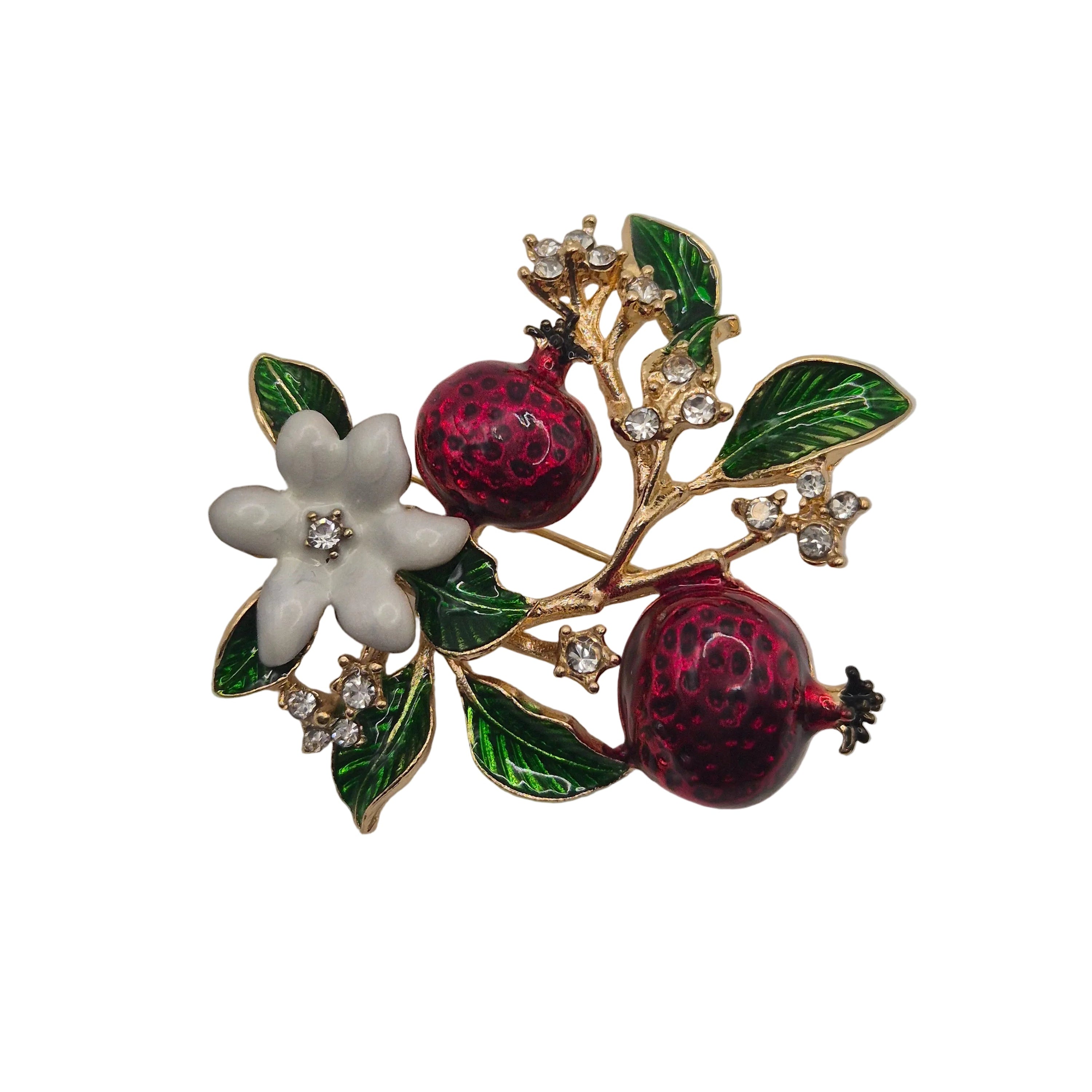 A gold-tone brooch featuring two glossy dark red pomegranate fruits, a white enamel flower, and green enamel leaves, accented with small clear rhinestones on a plain white background.
