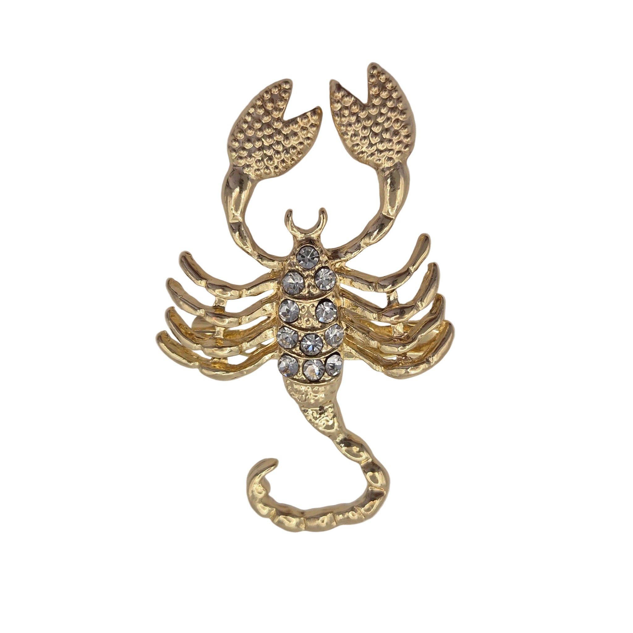 A gold-toned scorpion-shaped brooch or charm with clear rhinestones on its thorax, photographed on a plain white background.