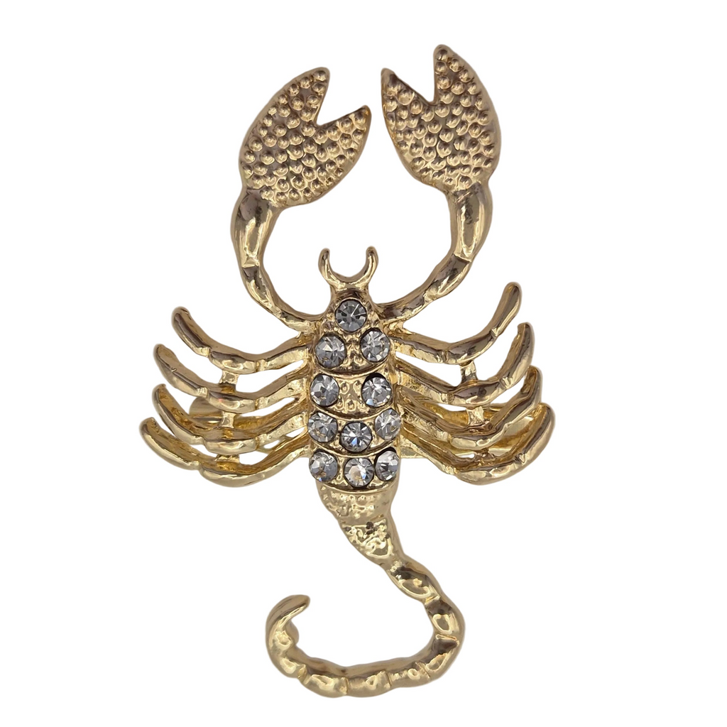 A gold-toned scorpion-shaped brooch or ring featuring a textured finish and a central cluster of clear rhinestones on a plain white background.