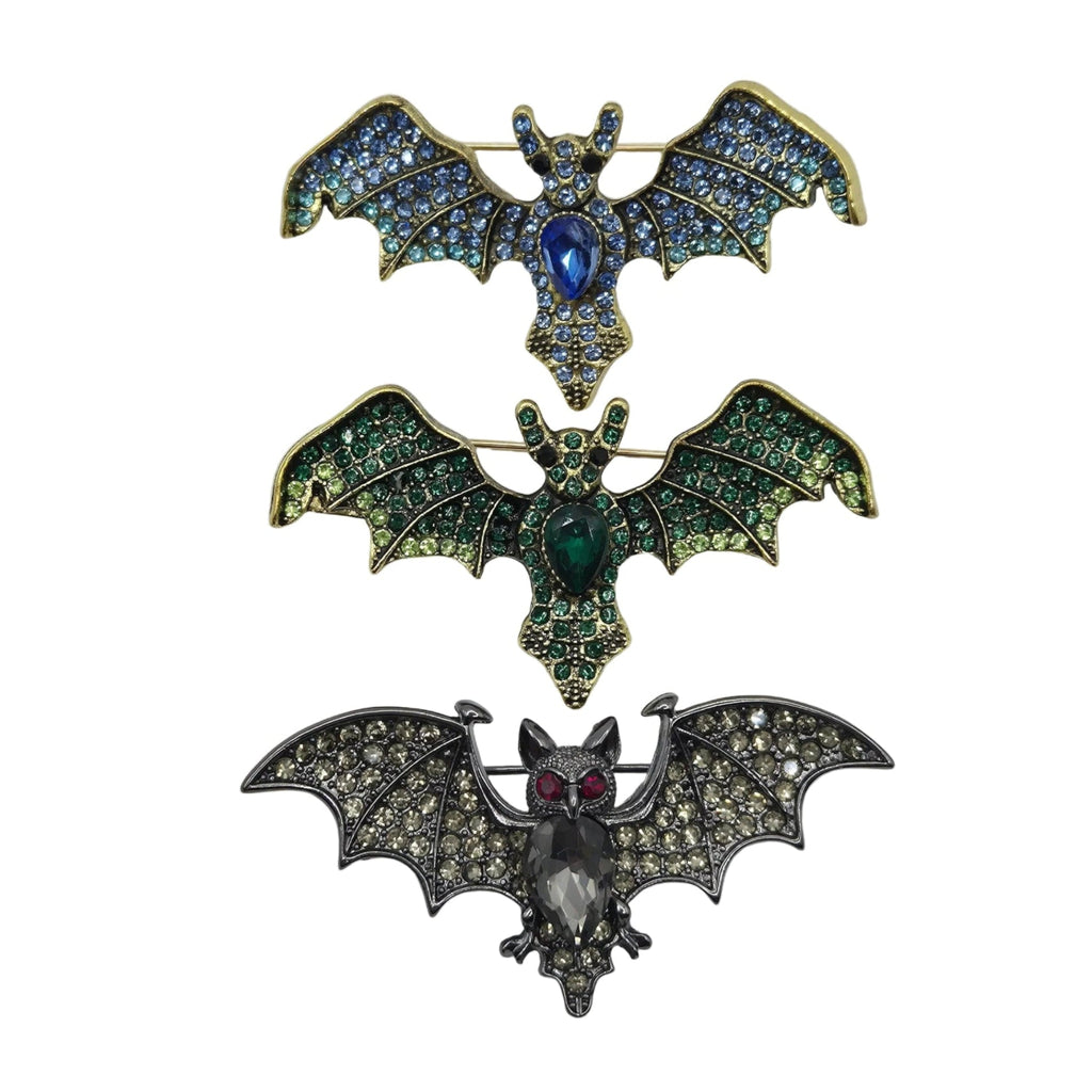Three bat-shaped brooches arranged vertically on a plain white background. The top brooch has blue and green rhinestones with a blue center stone and gold-tone edges.