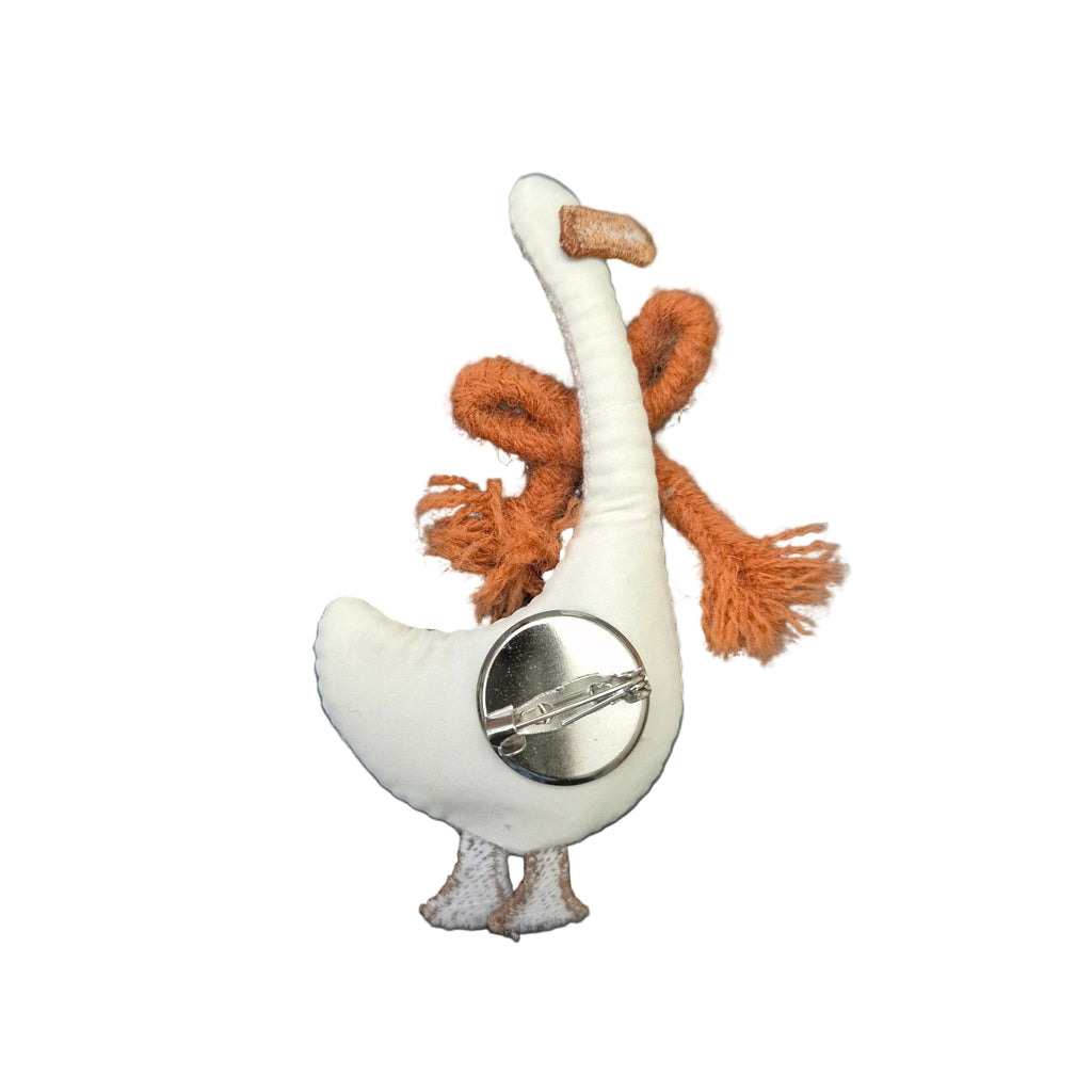 A small plush goose pin or brooch with a white body, orange-brown fluffy neck and tail, and a silver metal pin back, shown on a plain white background.