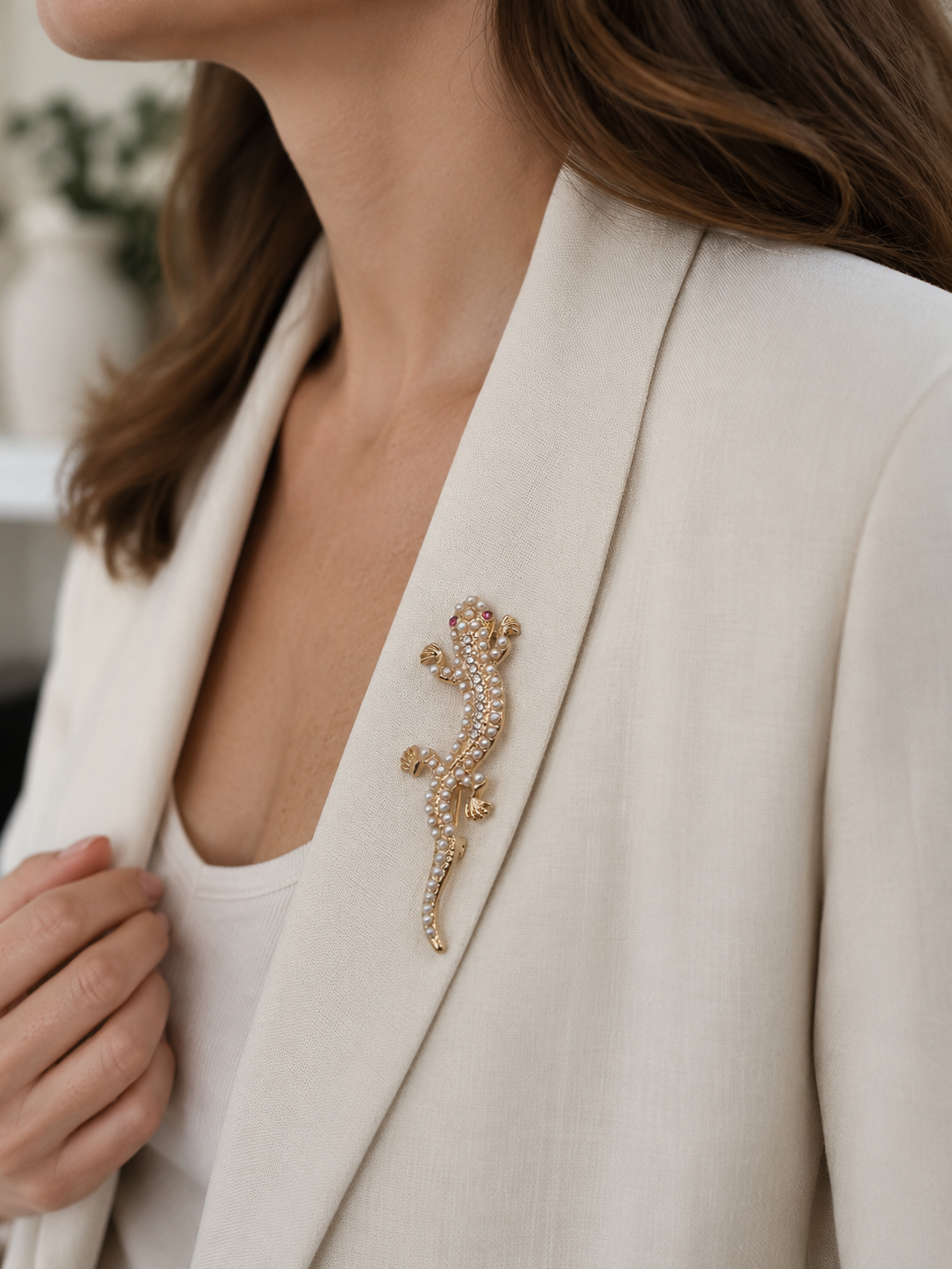 A close-up of a woman wearing a gold lizard-shaped brooch embellished with small clear rhinestones on her cream blazer.