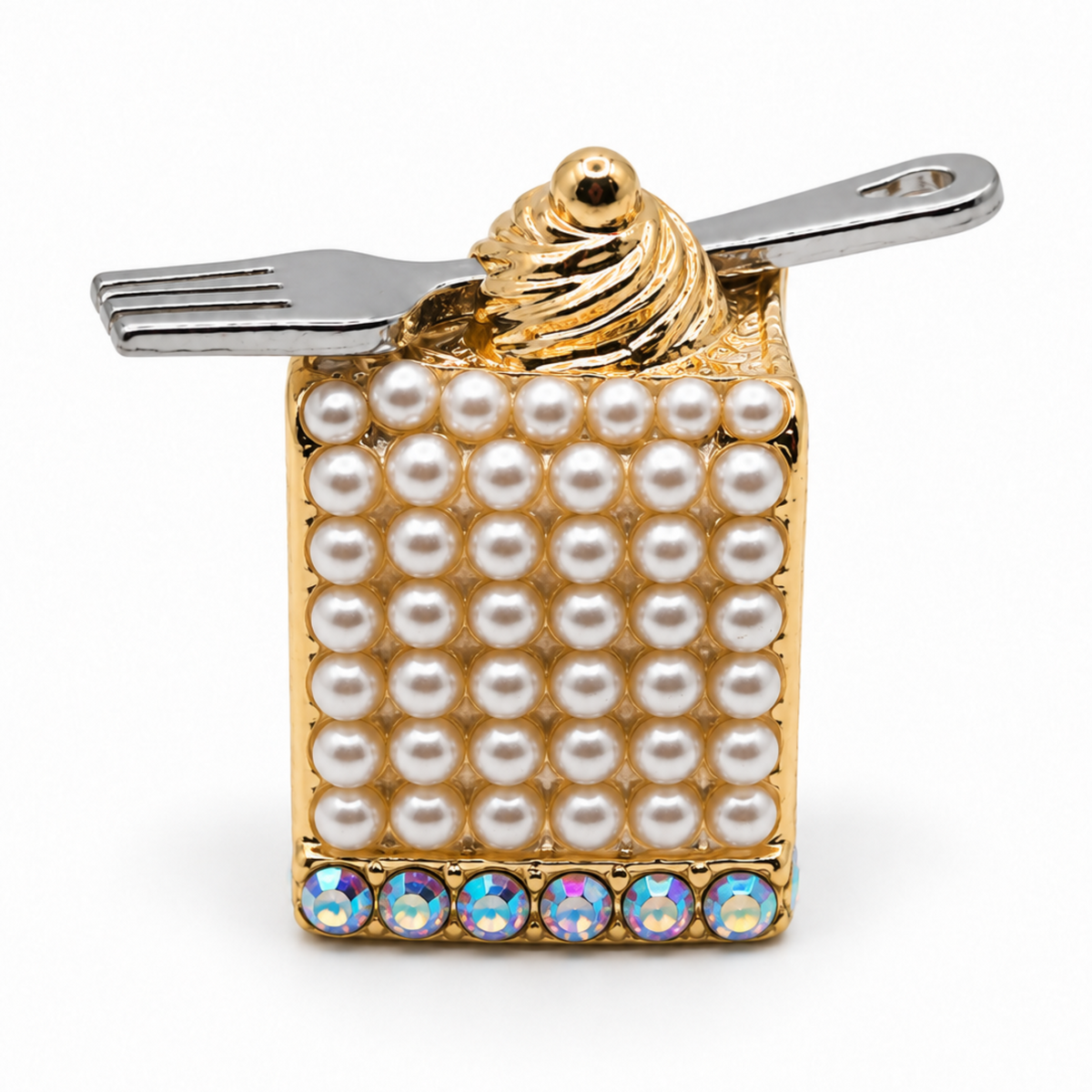 A novelty lapel pin shaped like a dessert cake with white faux pearls, a gold swirl top, a silver fork, and iridescent rhinestones along the bottom edge, shown on a white background.