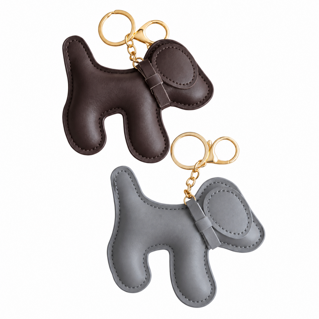 Two dog-shaped leather keychains, one dark brown and one light gray, both with gold-tone keyrings, shown on a plain white background.