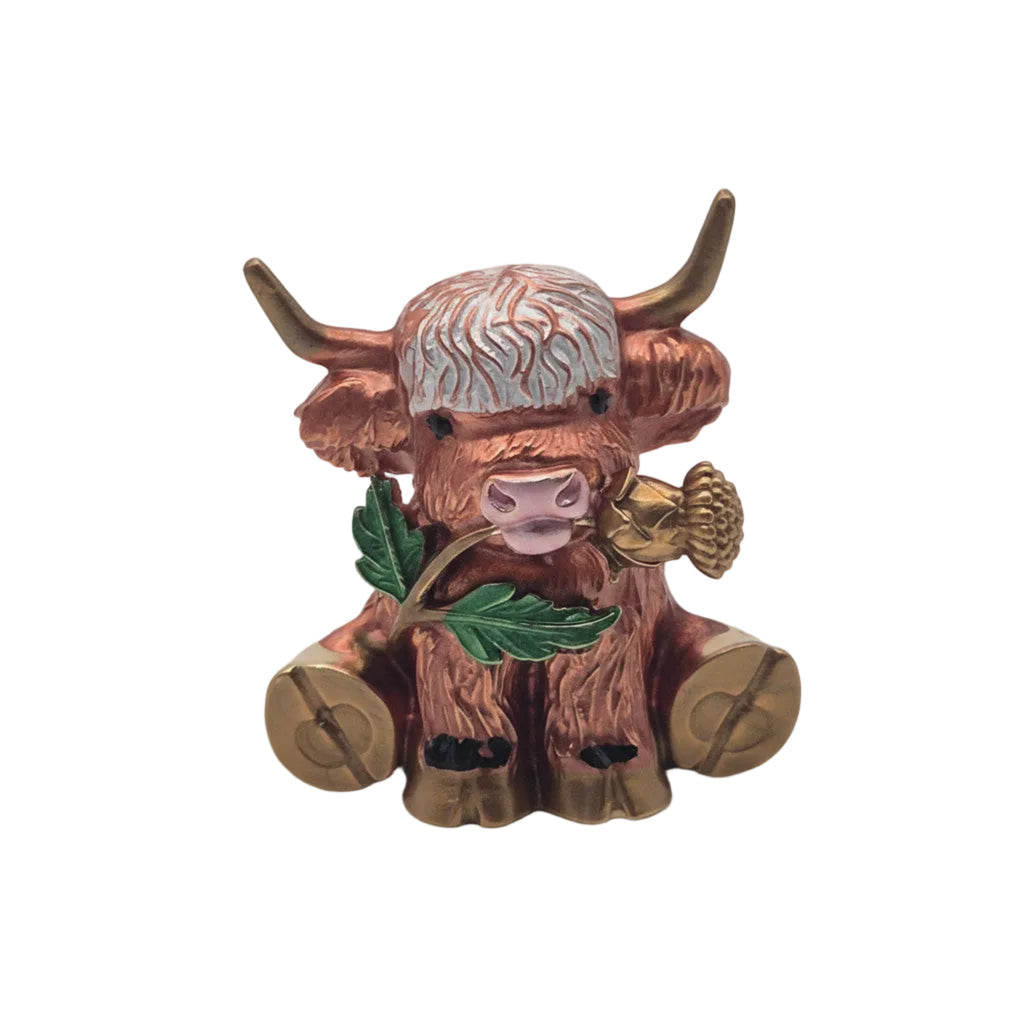 A Highland cow brooch with long horns, holding green leaves and flower, shown on a plain white background.