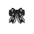 A black enamel bow pin decorated with white ghost motifs, shown on a plain white background.