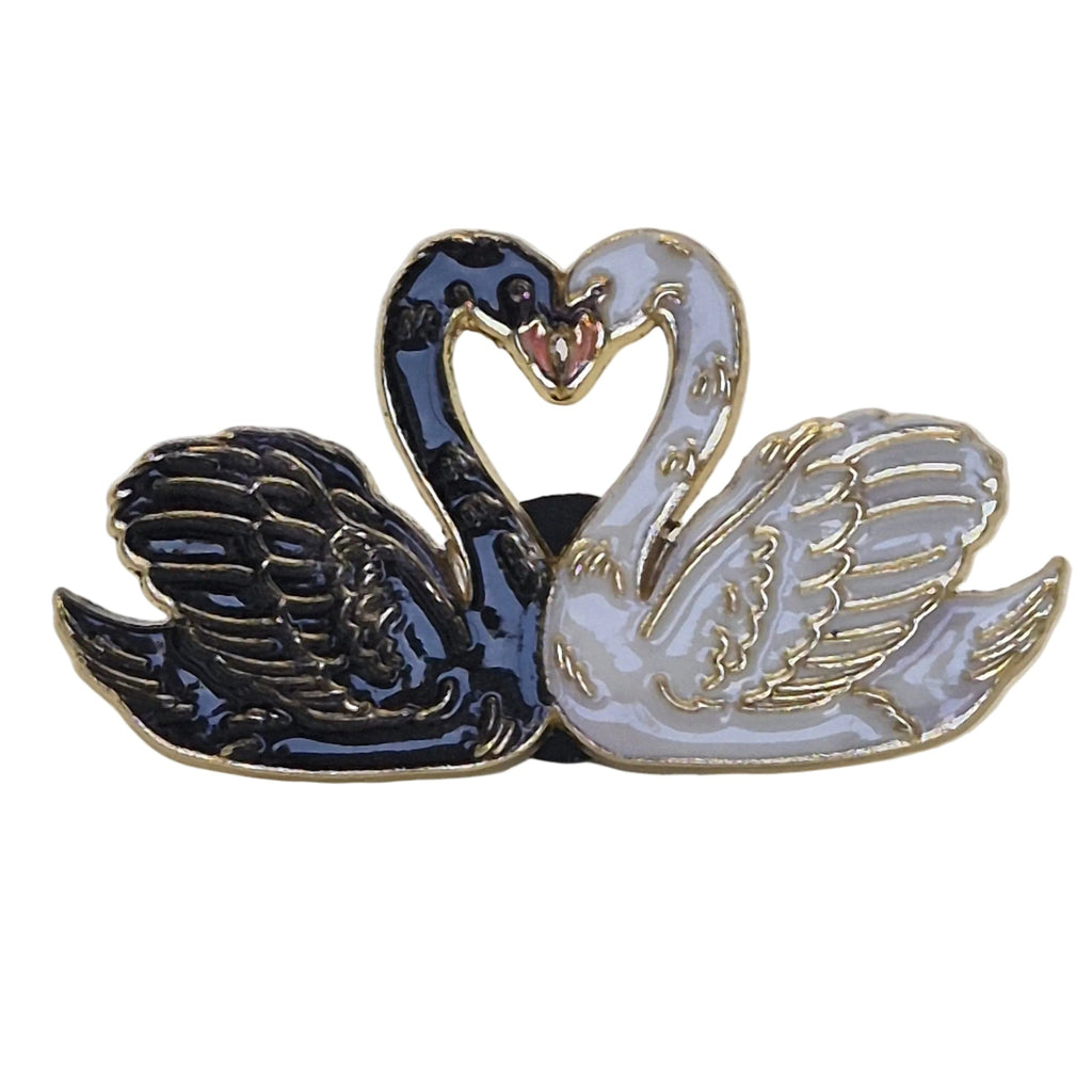 A twin swan enamel lapel pin featuring one black swan and one white swan facing each other in a heart-shaped pose with gold-tone metal outlines, set against a plain white background.