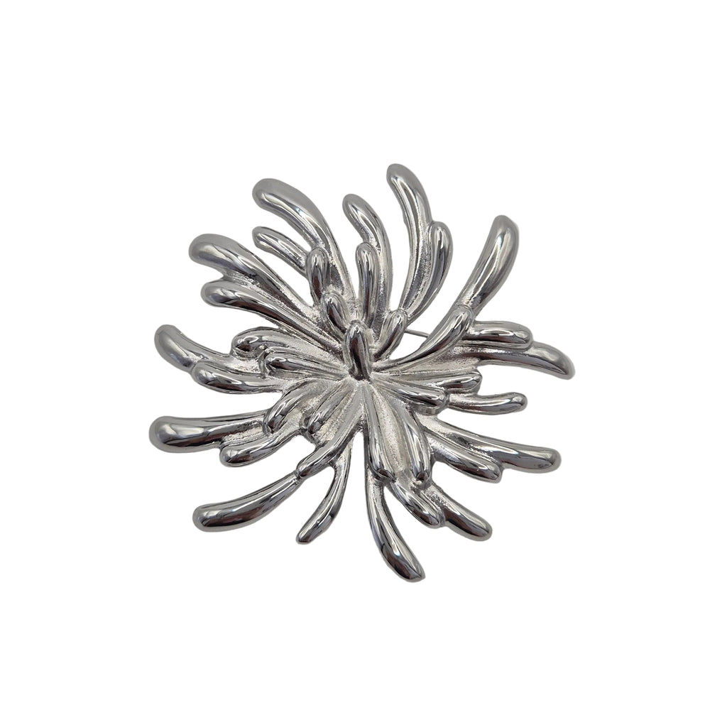 A silver metallic brooch shaped like a stylized firework burst, shown on a plain light gray background.