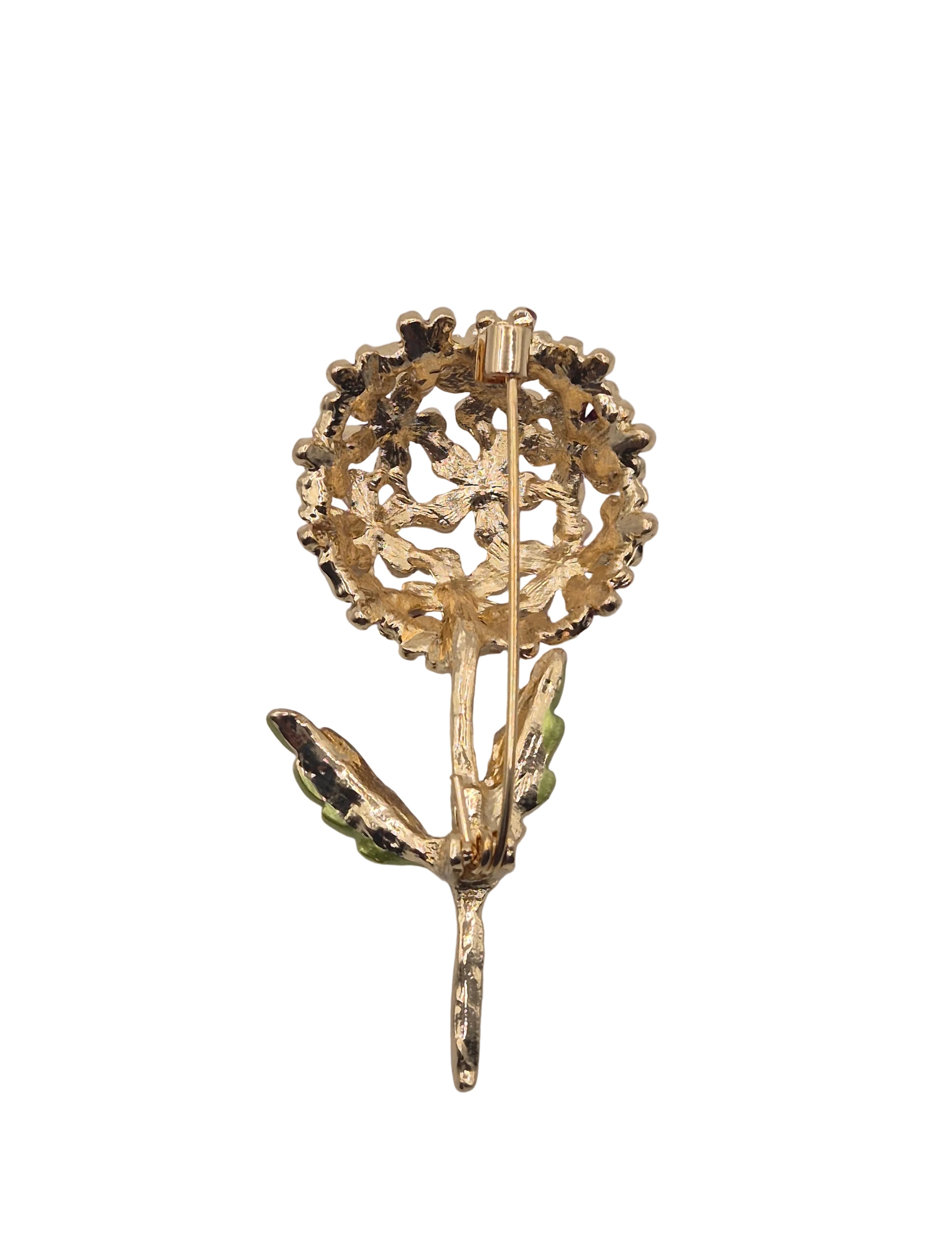 A vintage gold-tone flower brooch with green enamel accents on the stem and leaves, set against a plain white background.