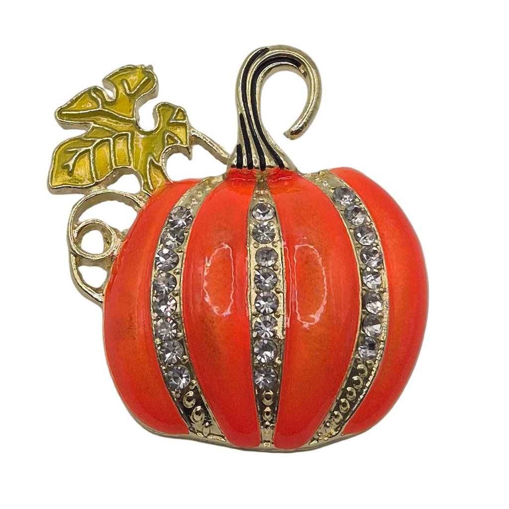 A pumpkin-shaped brooch with a glossy orange-red enamel body, gold-tone metal trim, clear rhinestones, and a gold vine and leaf detail on a white background.