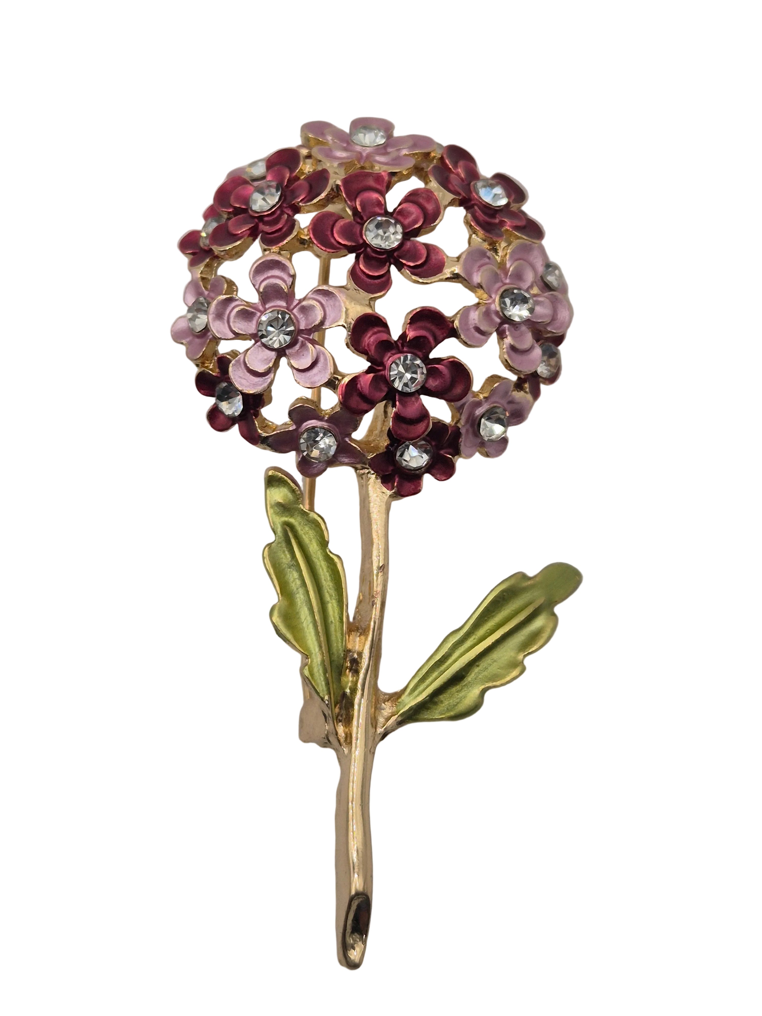 A vintage-style floral brooch featuring a cluster of small flowers with pink, burgundy, and lilac enamel petals, clear rhinestones, and olive green leaves on a gold-tone stem, shown against a plain white background.