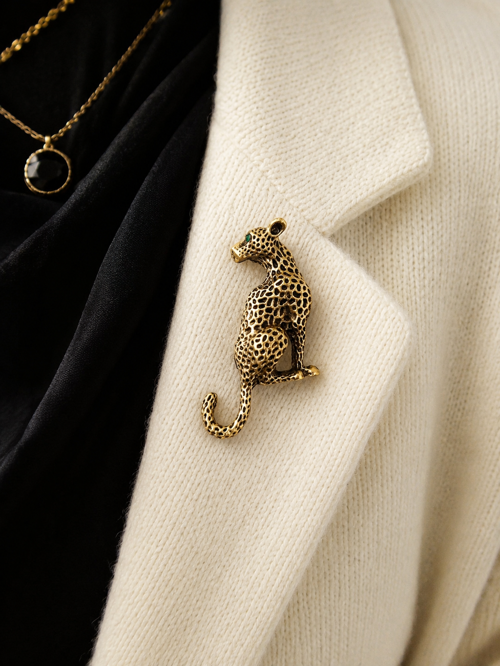 A gold-toned leopard-shaped brooch pinned to a cream knit cardigan over a black garment, with part of a gold necklace visible.