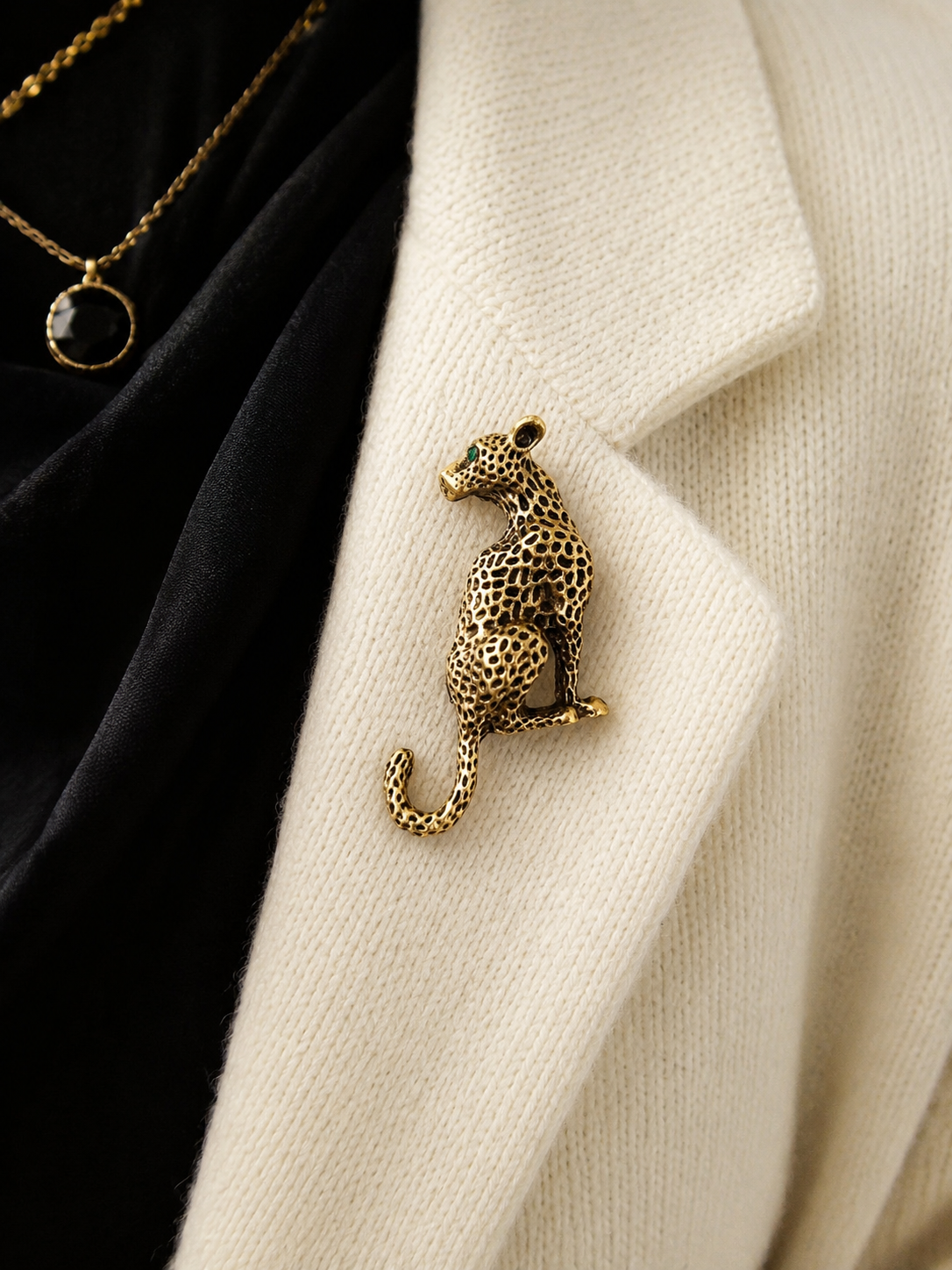 A gold-toned leopard-shaped brooch pinned to a cream knit cardigan over a black garment, with part of a gold necklace visible.