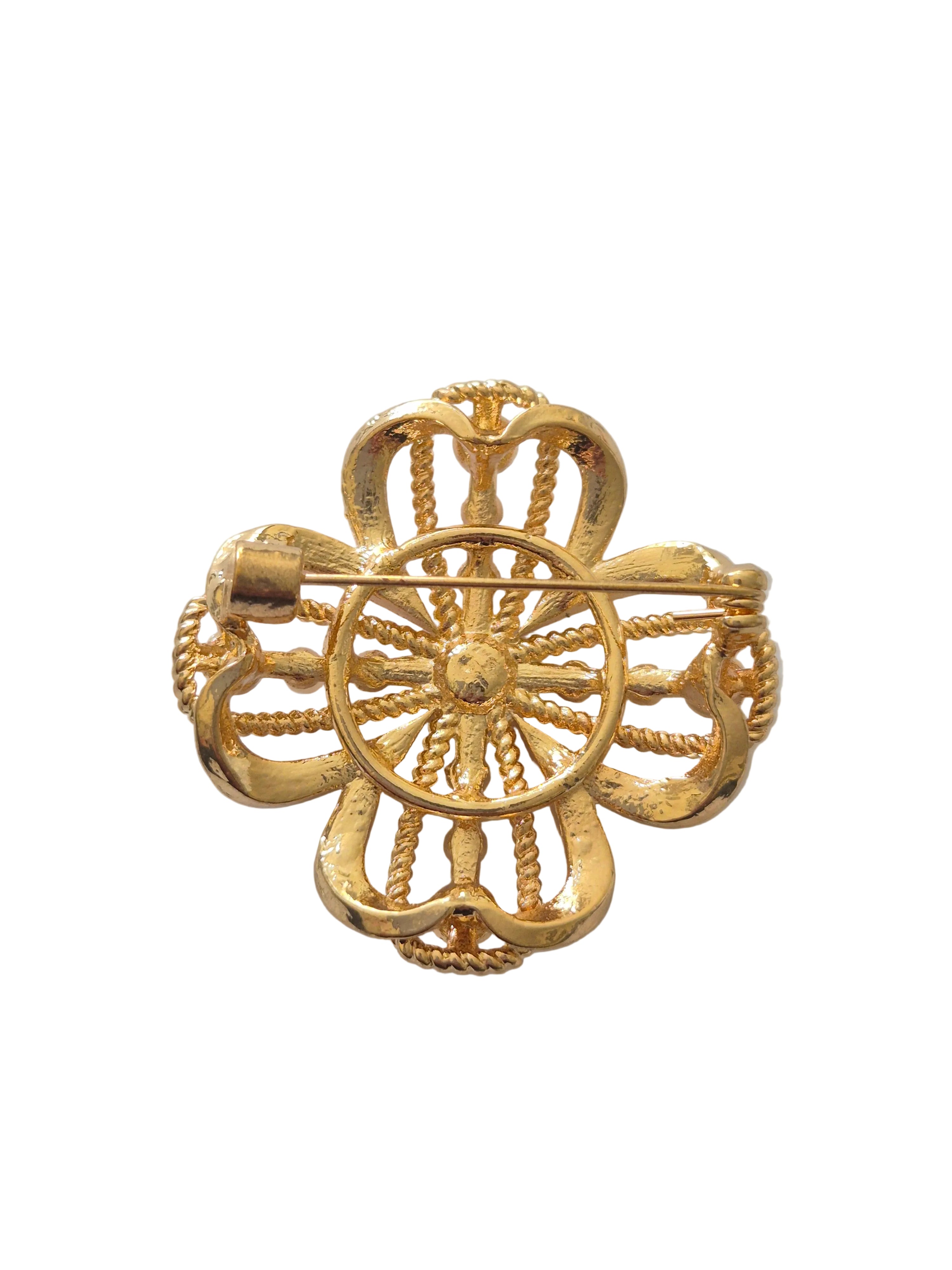 four-leaf clover brooch with central gemstone on a light gray background