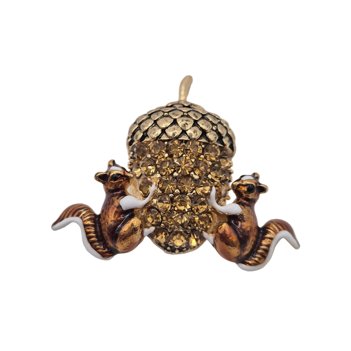 A vintage-style gold tone brooch or pendant featuring two small squirrels flanking a large acorn embellished with rhinestones, set against a plain white background.